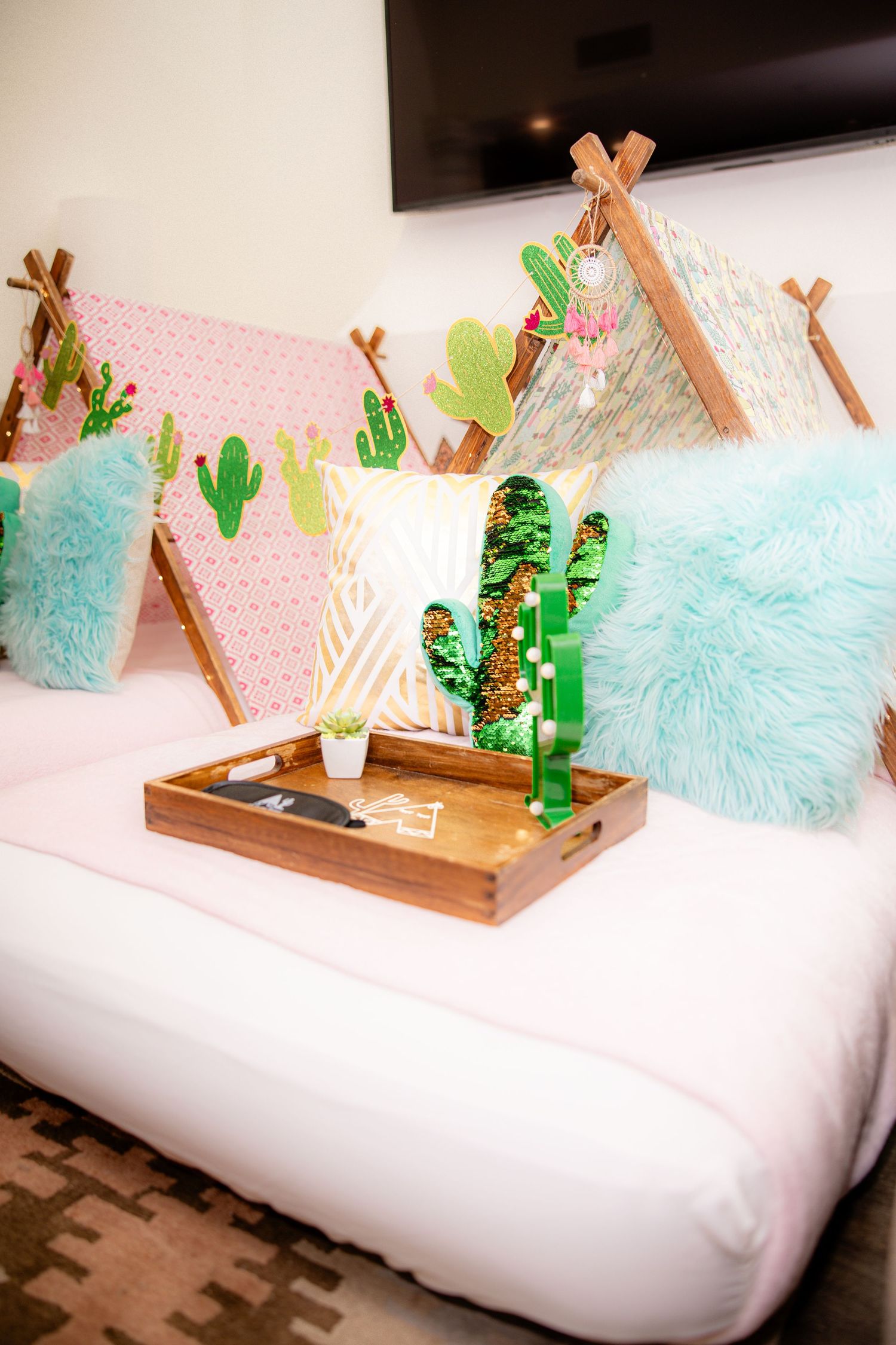 Colorful kids sleepover setup with cactus-themed teepees, fluffy pillows, and a wooden tray.