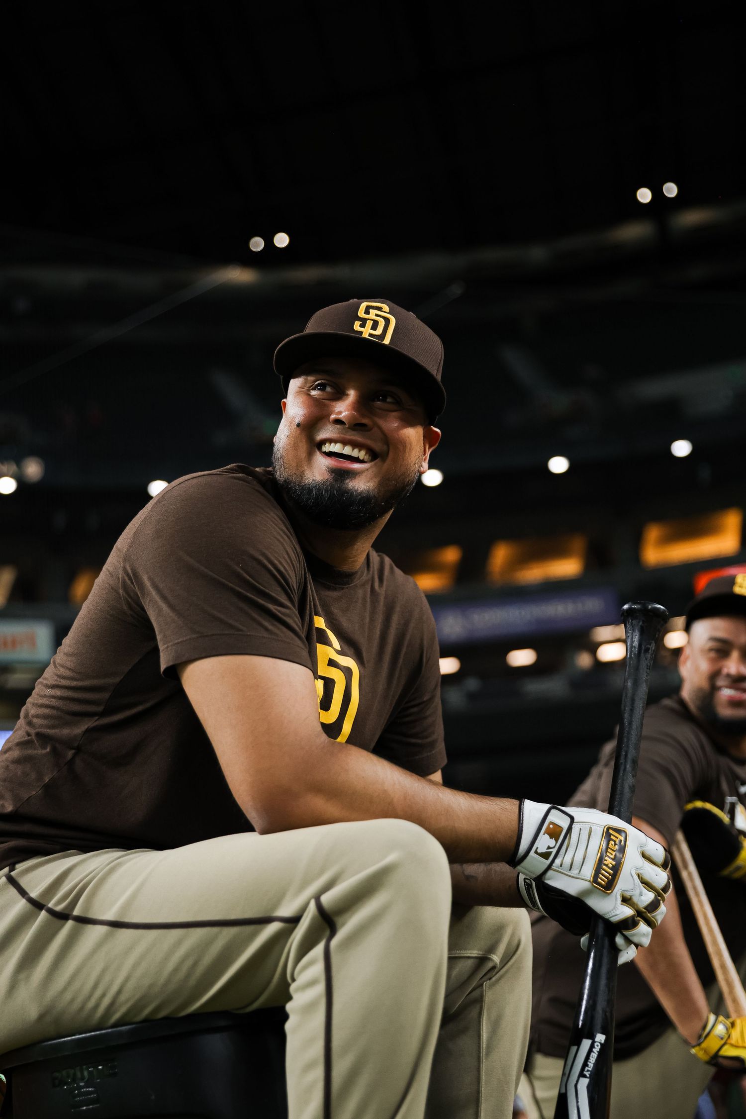 San Diego Padres player smiles while holding a bat in the dugout during a baseball game.