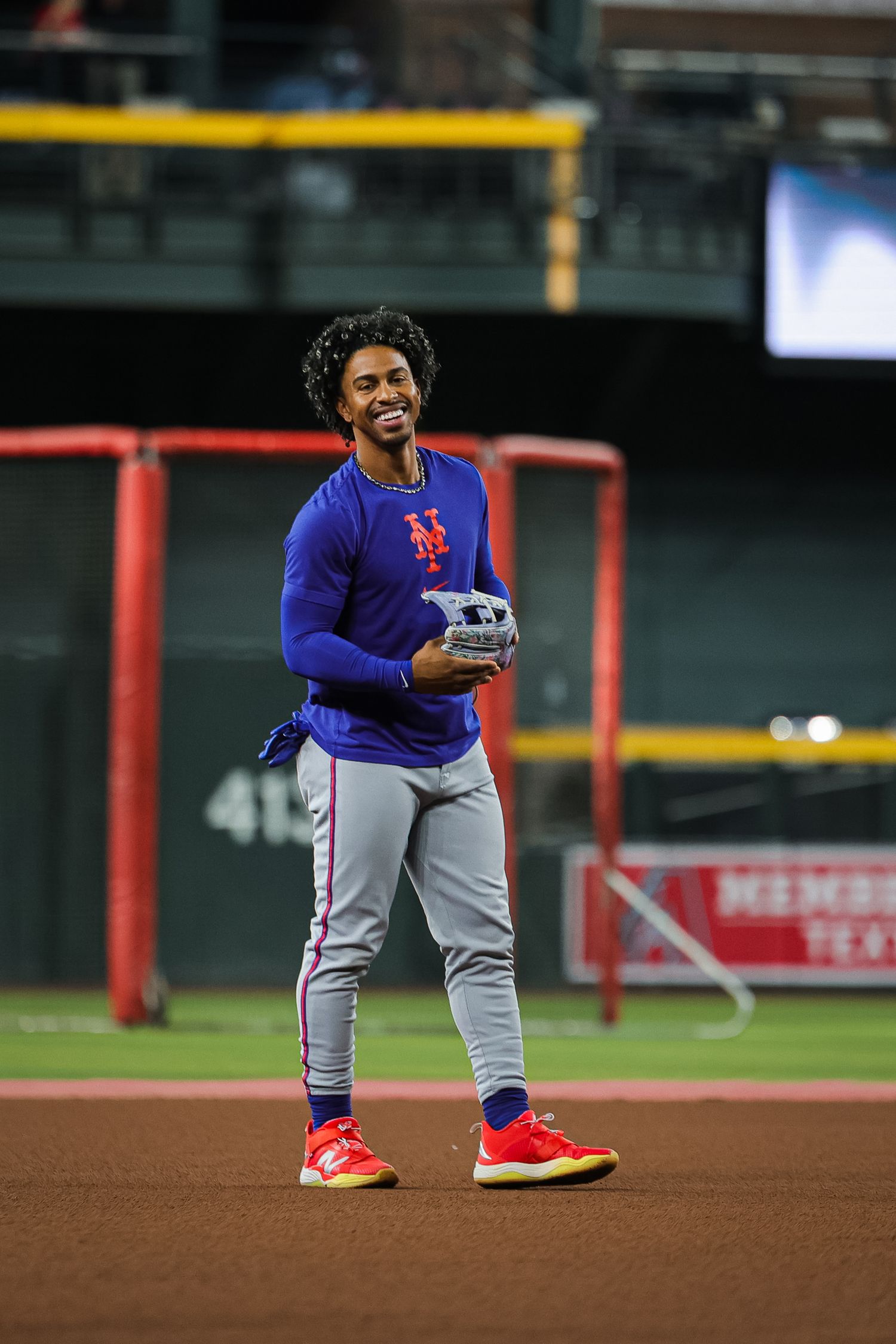 New York Mets player smiles while holding glove during pre-game warmups at stadium.