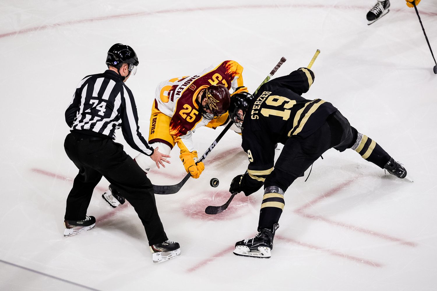 ASU hockey player faces off against an opponent as a referee drops the puck on ice.