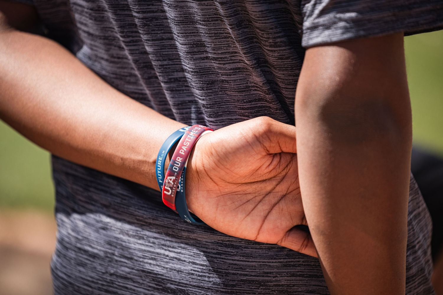 Close-up of an athlete's wrists with colorful wristbands crossed behind their back outdoors.