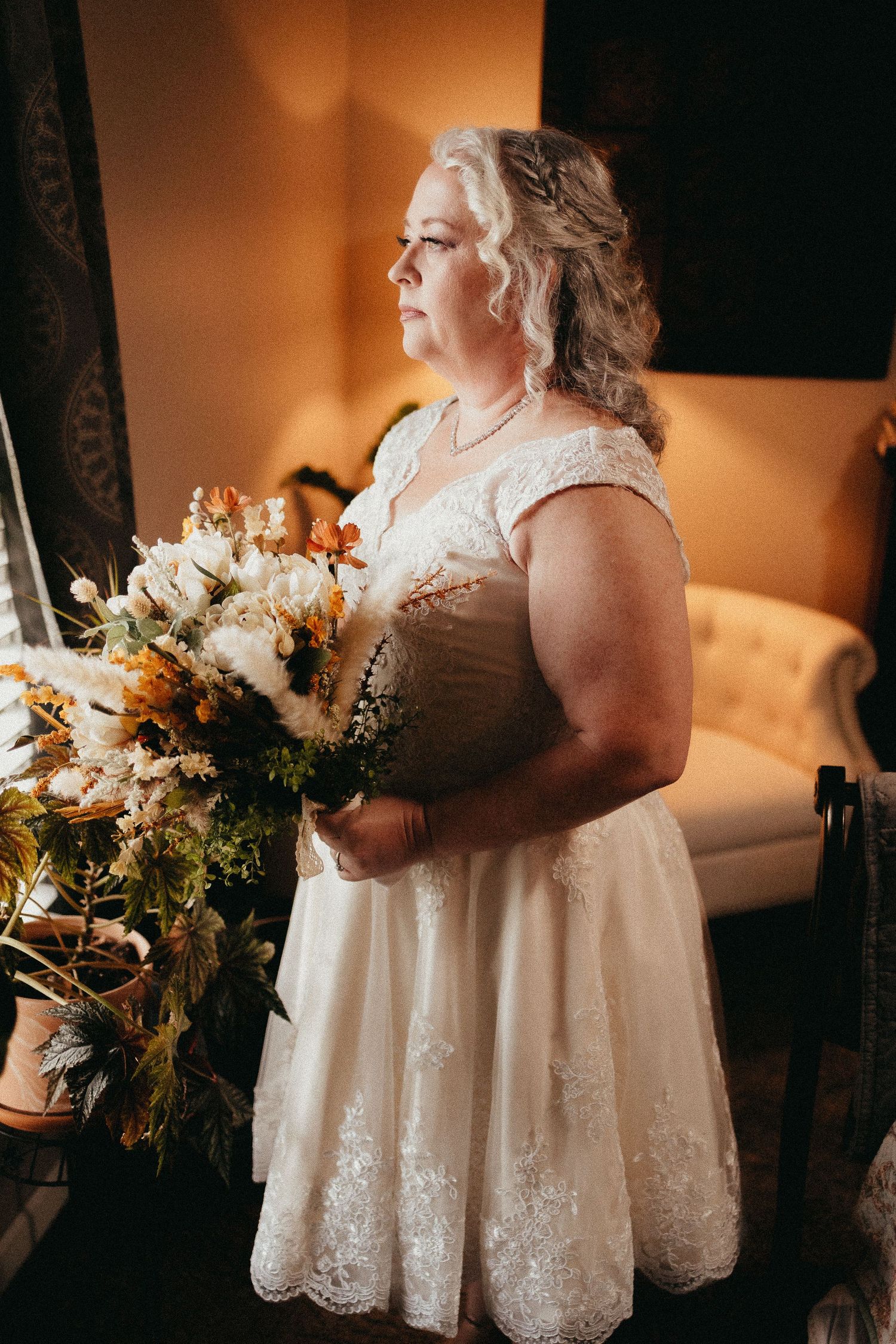Plus size bride in lace wedding dress holding autumn bouquet of white and orange flowers.