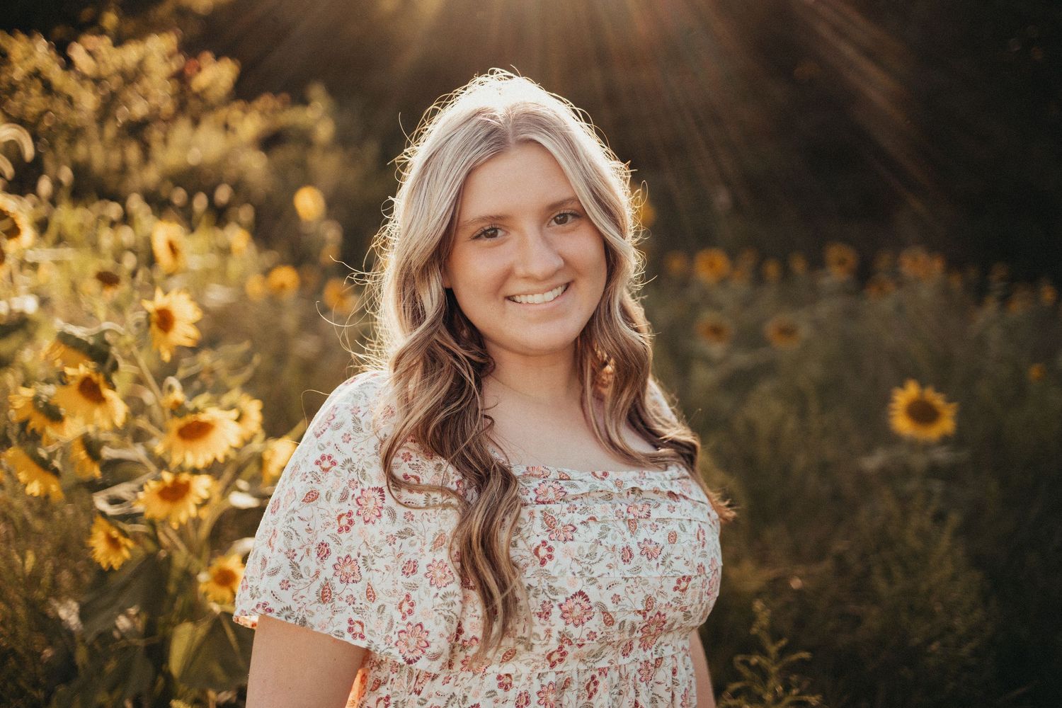 Smiling young woman with wavy hair posing in a sunflower field during golden hour.