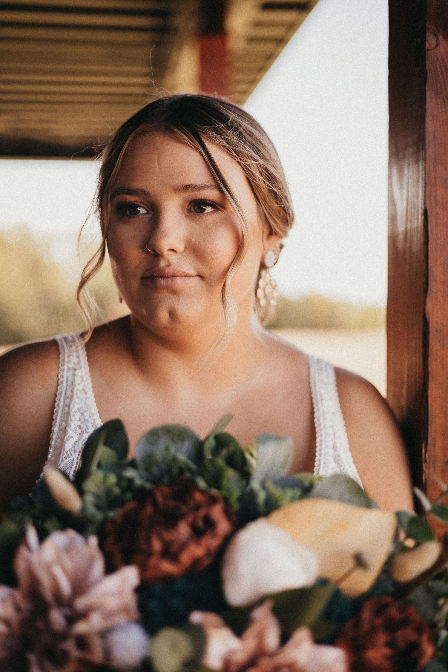 Close-up portrait of bride holding lush bouquet with dahlias and greenery in warm golden light.