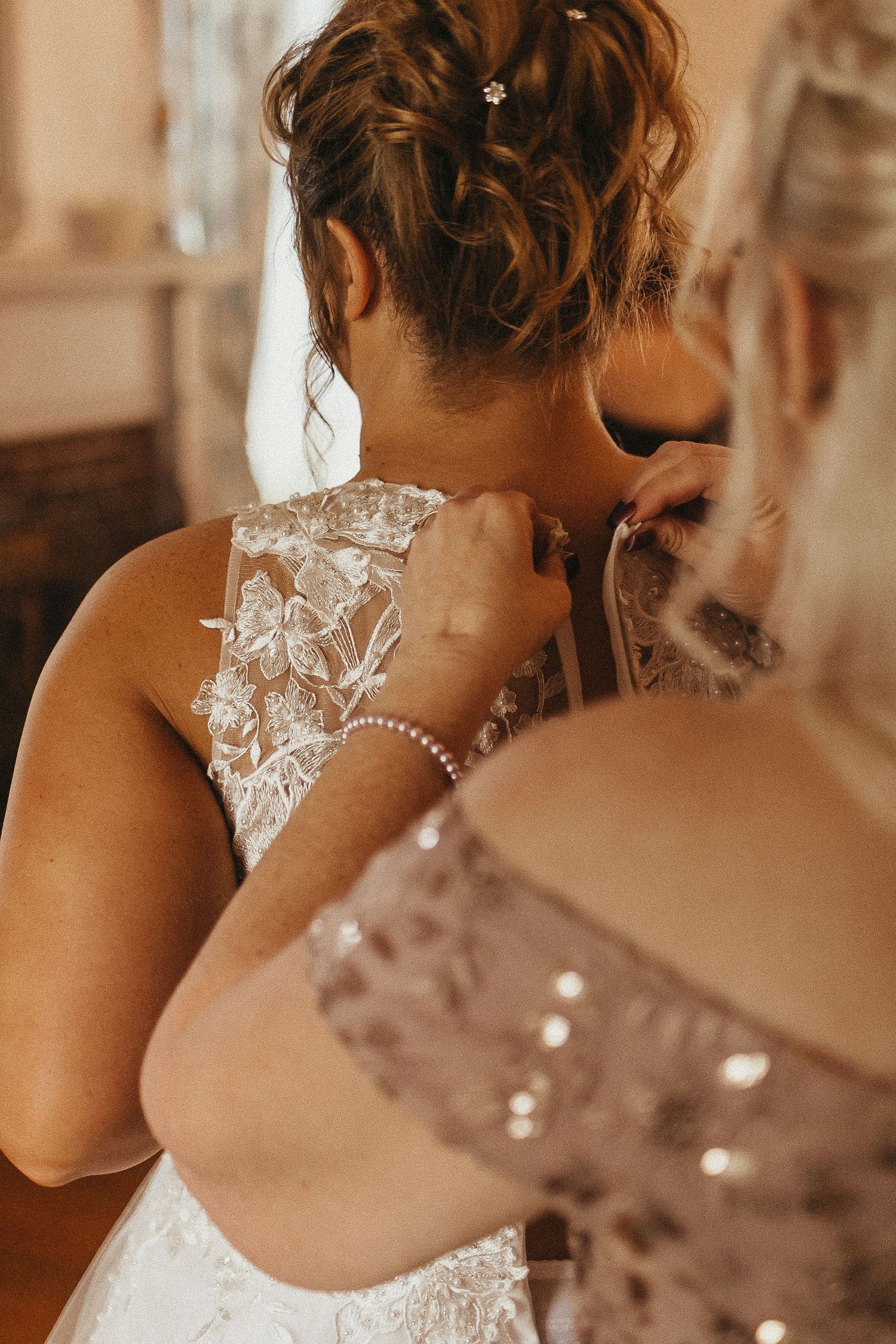 Close-up of a helper fastening the back of a bride's intricate lace wedding dress with butterfly embroidery details.