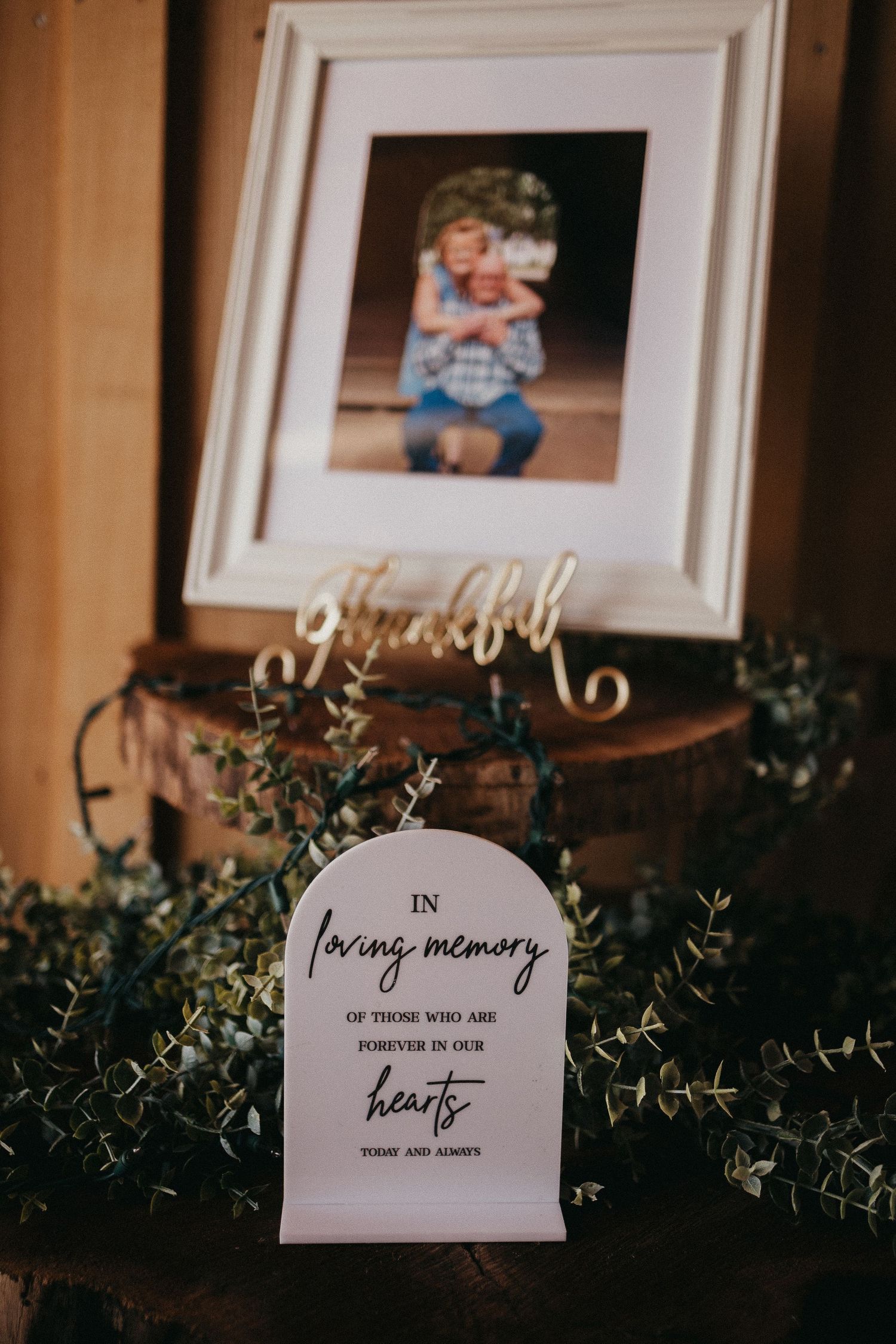 Wedding memorial display with framed photo, greenery, and arch sign reading In Loving Memory of those forever in our hearts.