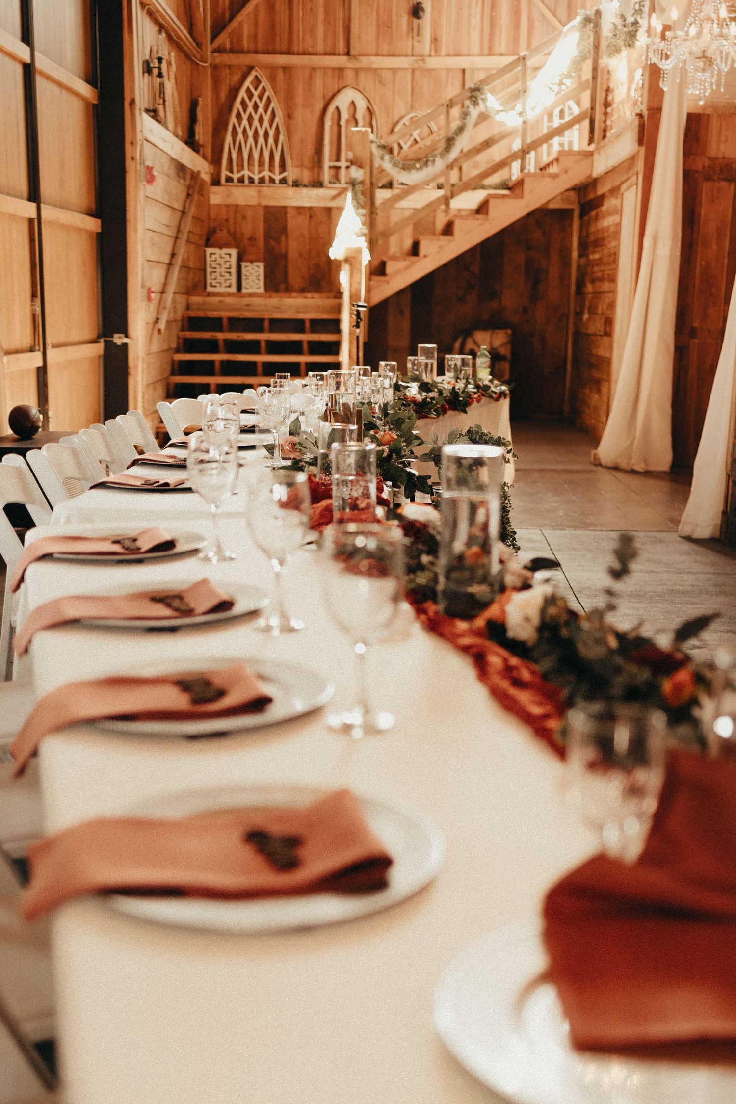 Rustic barn wedding reception table with terracotta napkins, floral centerpieces, and candlelight decor.