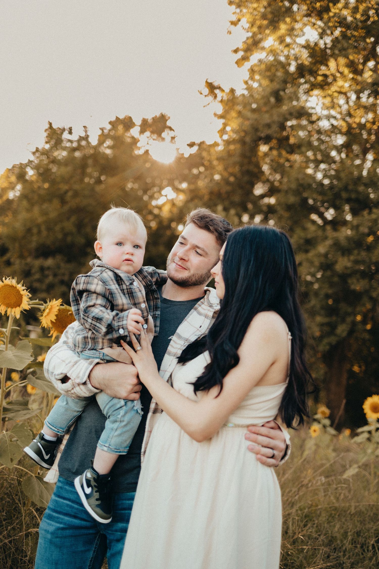 Happy family with a toddler posing in a sunflower field during golden hour sunset.