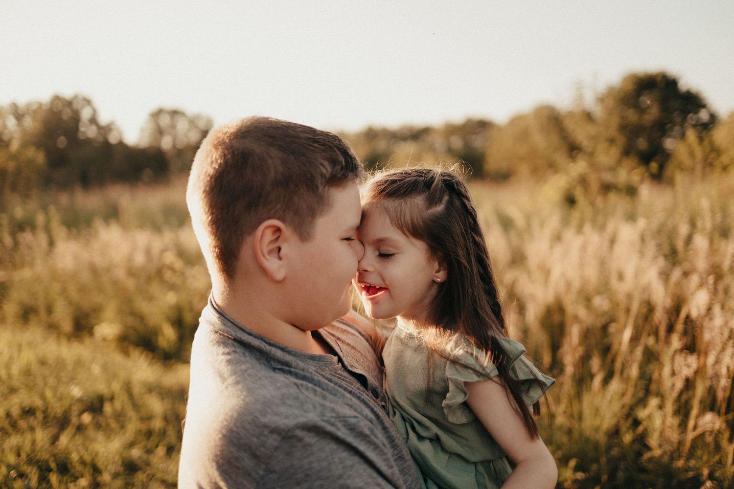 Boy and little girl touching foreheads affectionately in a sunny meadow.