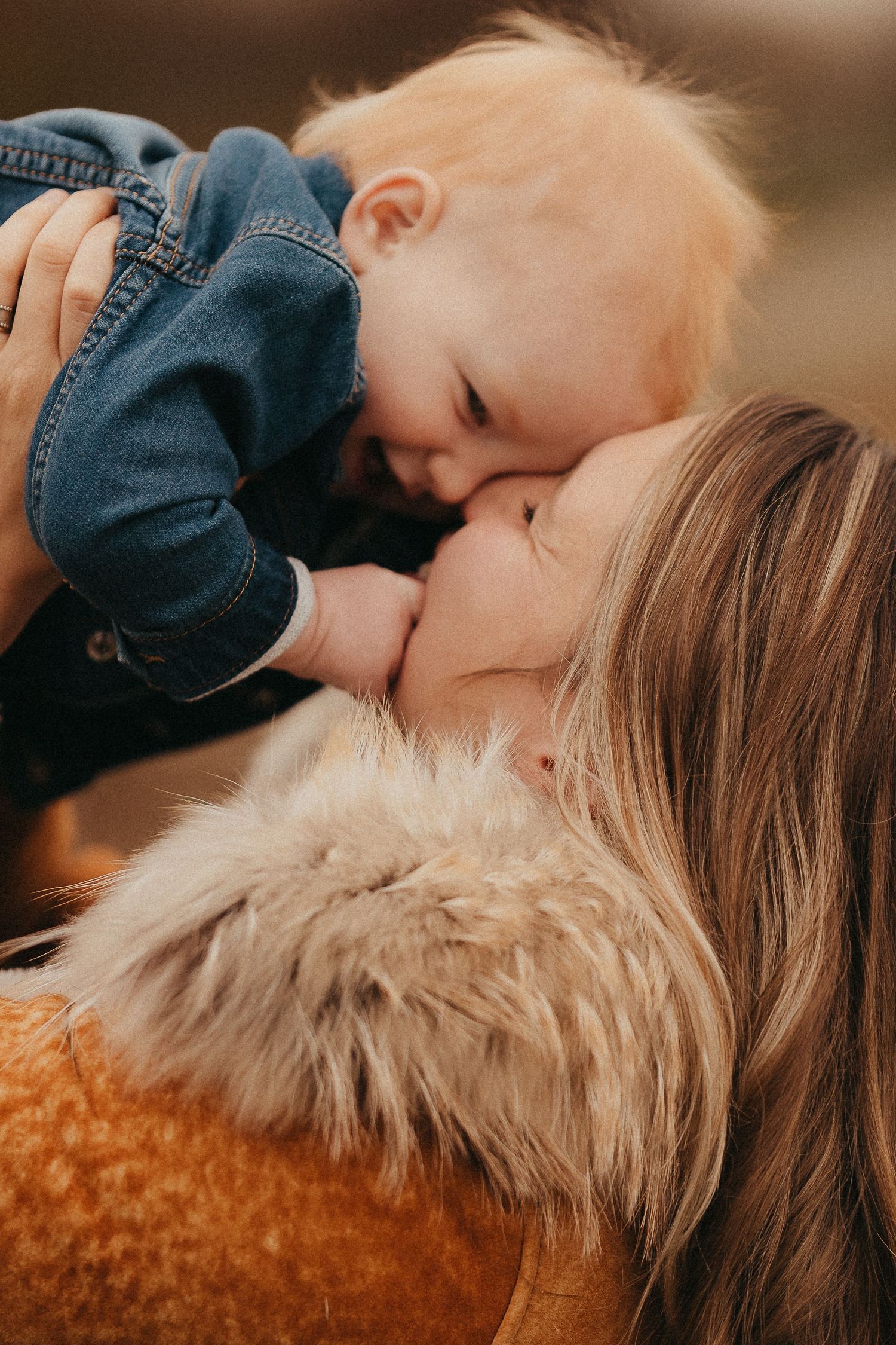 Mother tenderly kissing her red-haired baby while holding him up close in a warm outdoor setting.