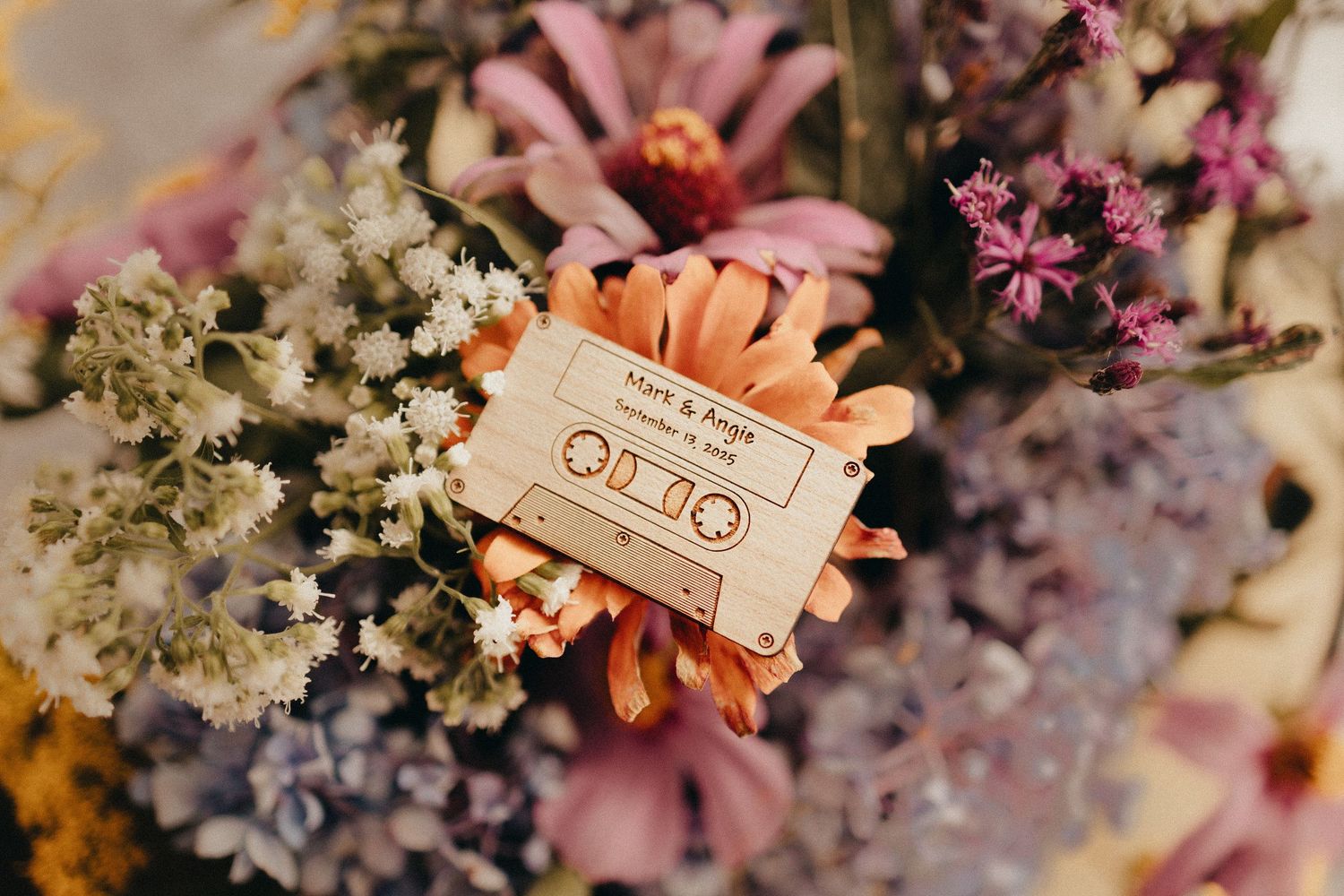 Wooden cassette tape keepsake rests among colorful wildflower wedding bouquet with pink and orange blooms.
