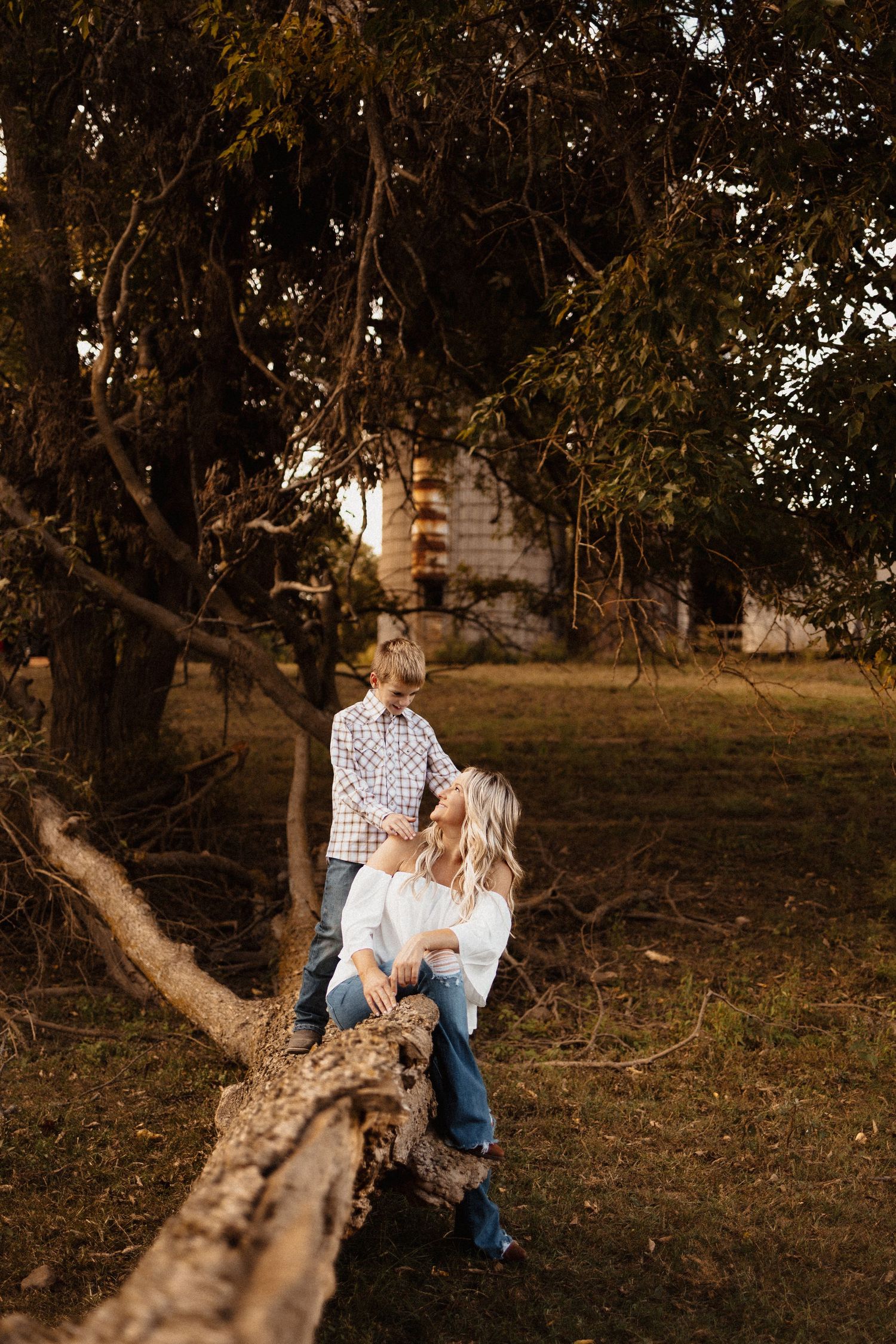 Mother and son sharing a tender moment together on a fallen tree in a rustic outdoor setting.