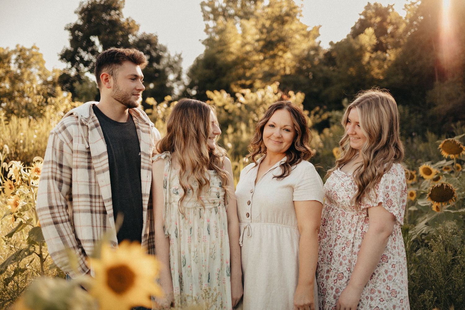 Family of four smiling together in a sunflower field during warm golden hour photography session.
