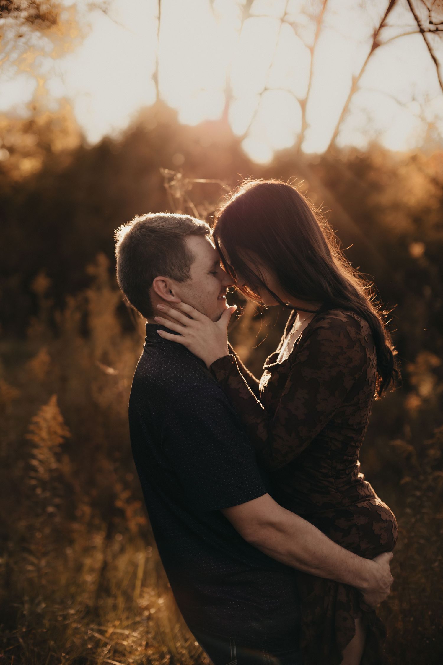 Couple embracing and touching foreheads in a golden sunset field, a romantic engagement photo with warm backlight and soft autumn tones.