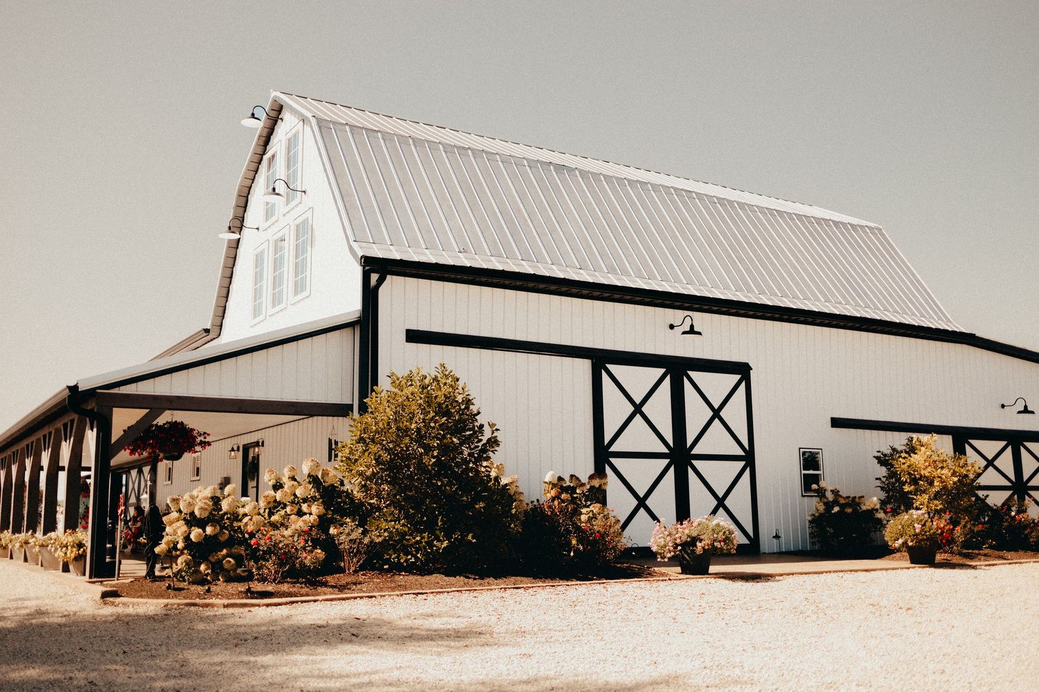 White modern barn wedding venue exterior with black trim under clear blue sky.