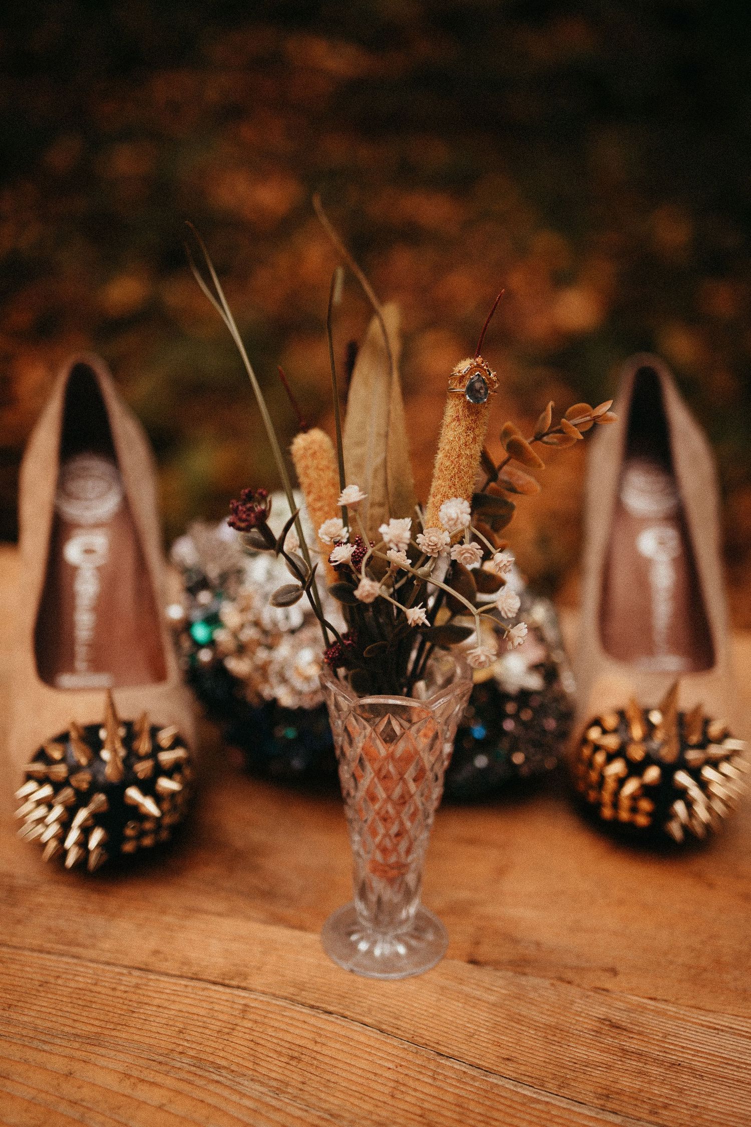 Ornate beaded bridal heels with small dried flower arrangement in crystal vase on wood table.