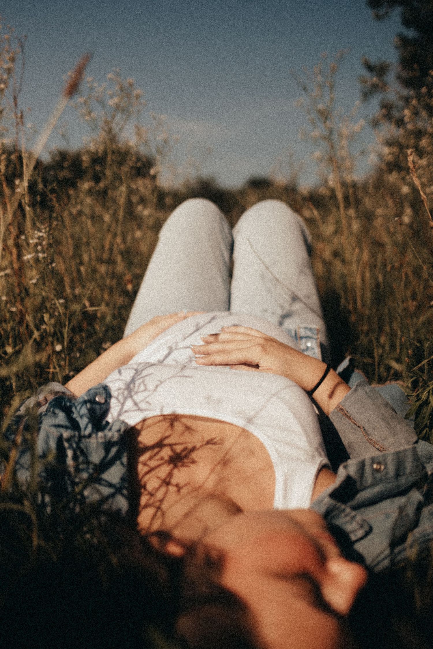 Pregnant woman lying in tall grass cradling her baby bump in warm sunlight.