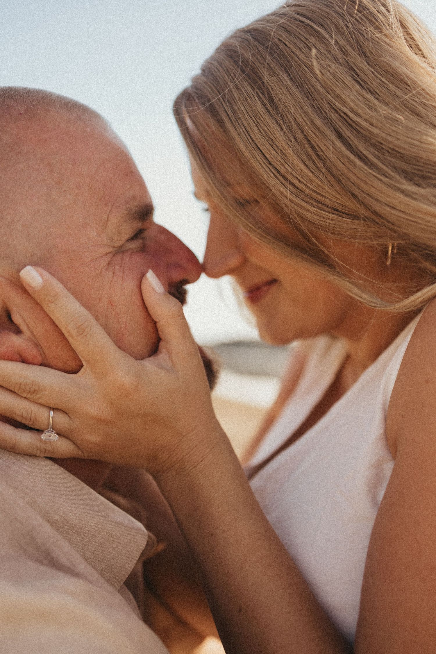 A couple shares a tender romantic moment, nearly kissing, woman wearing an engagement ring on her hand.
