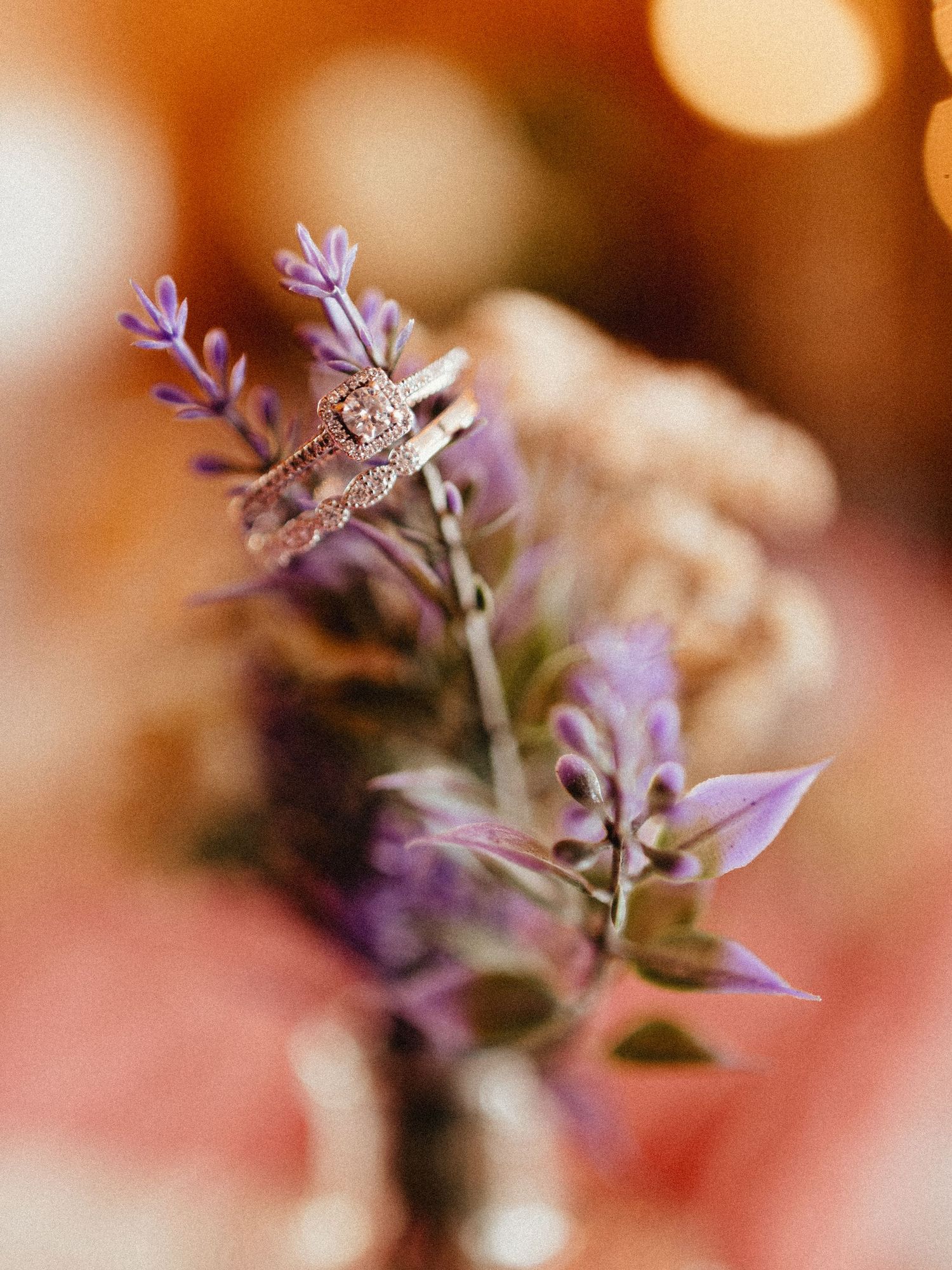 Elegant diamond engagement ring and wedding band displayed on purple lavender stems with bokeh background.