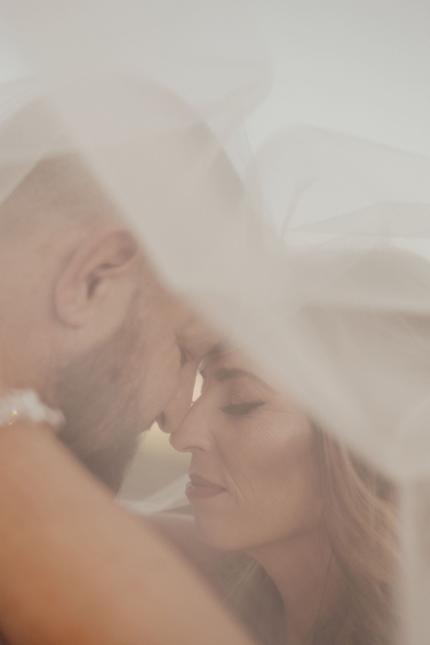 Intimate close-up of bride and groom nearly kissing under a flowing white veil.