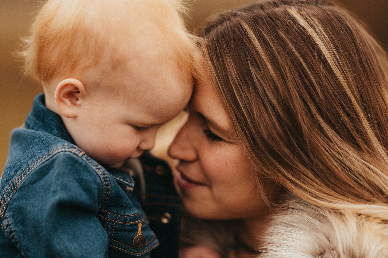 A tender moment between a mother and her red-haired baby touching foreheads and smiling outdoors.