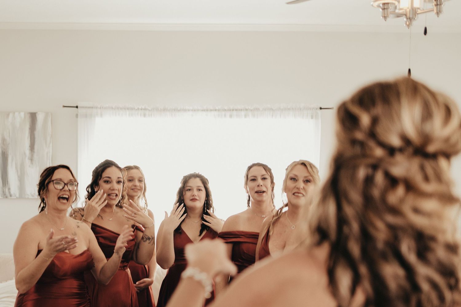 Bridesmaids in rust-colored dresses reacting with joy and tears to bride during first look.