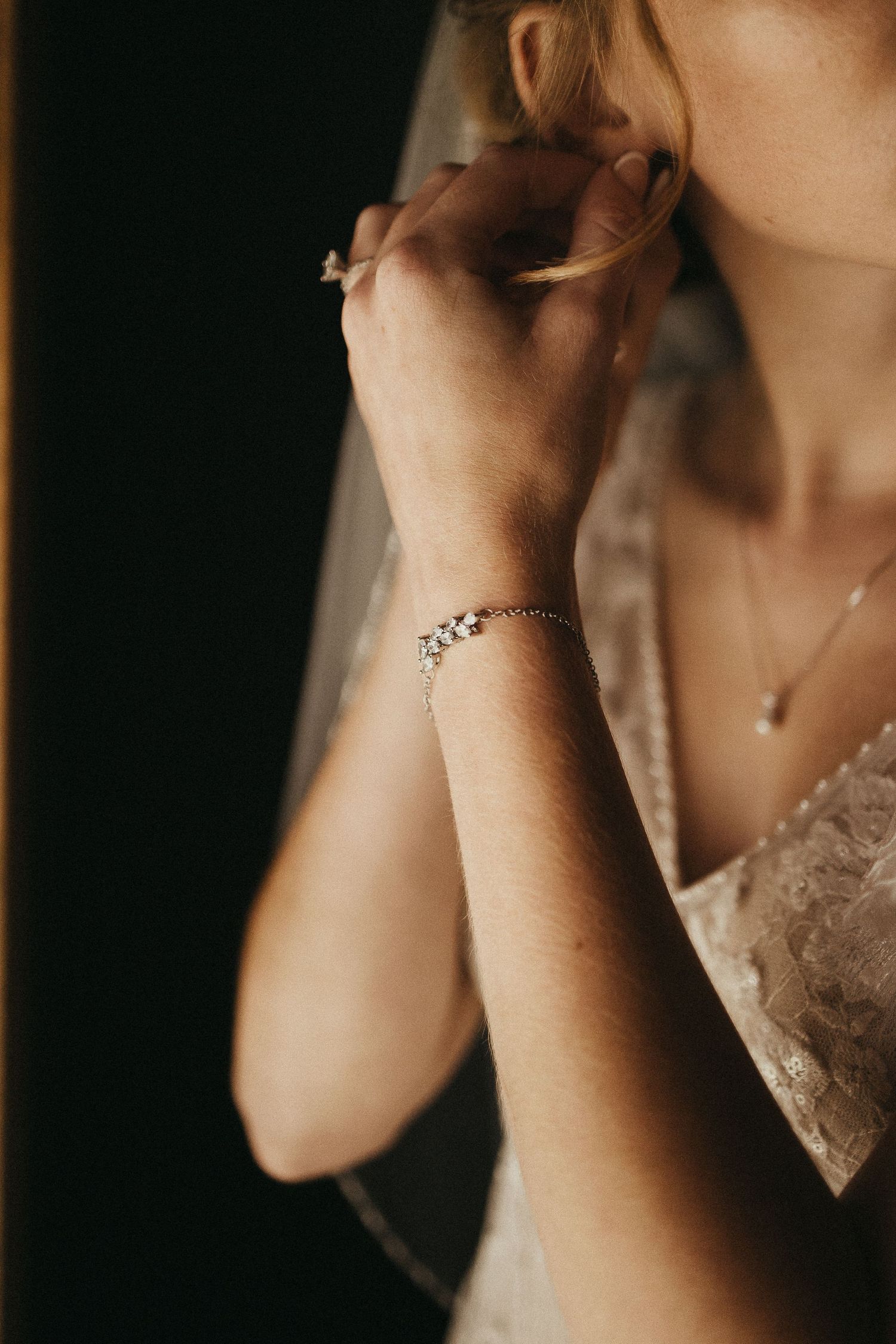 Detail shot of bride putting on earring wearing diamond bracelet and lace wedding gown with veil.