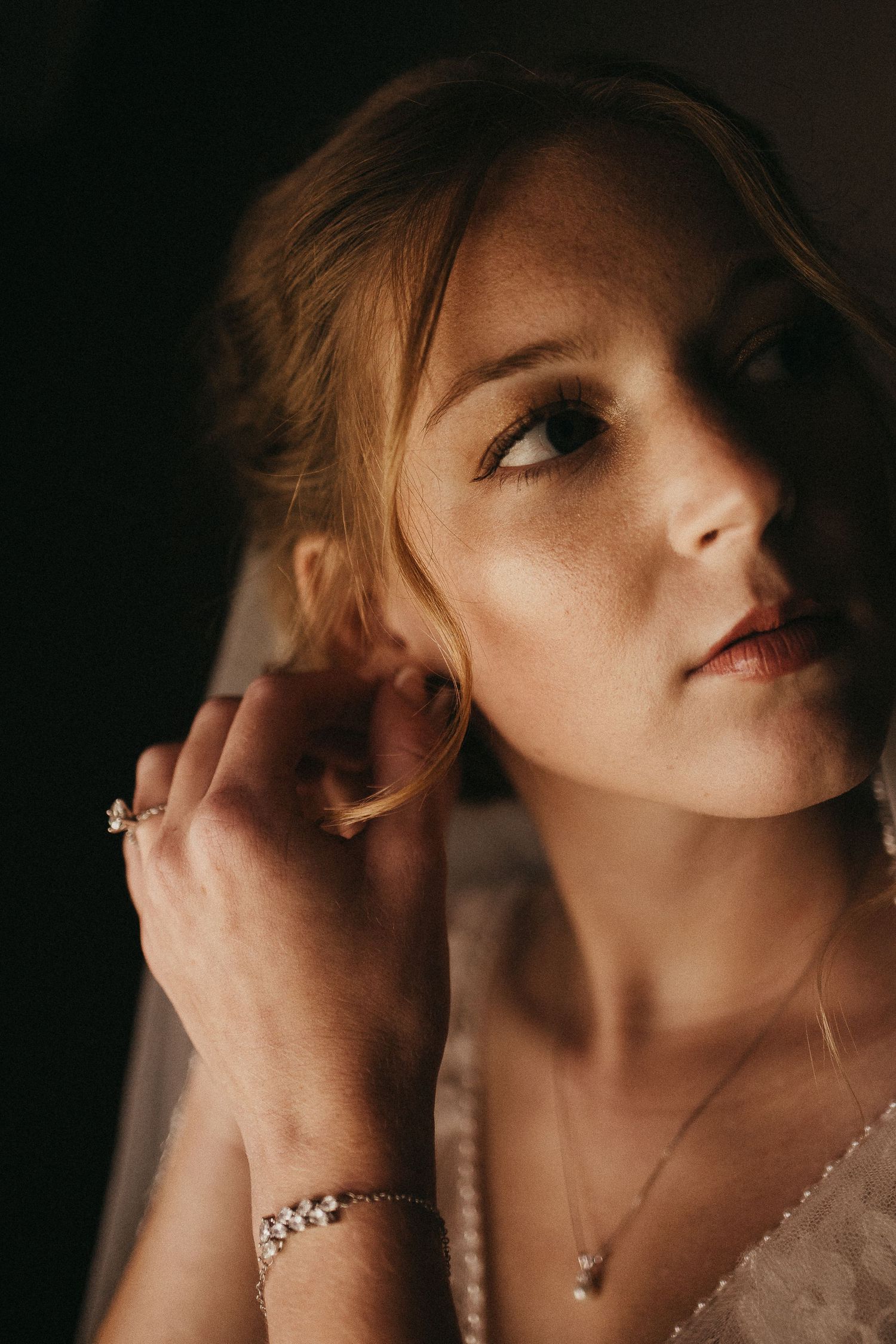 Close-up portrait of freckled bride adjusting earring wearing pearl bracelet and delicate necklace.
