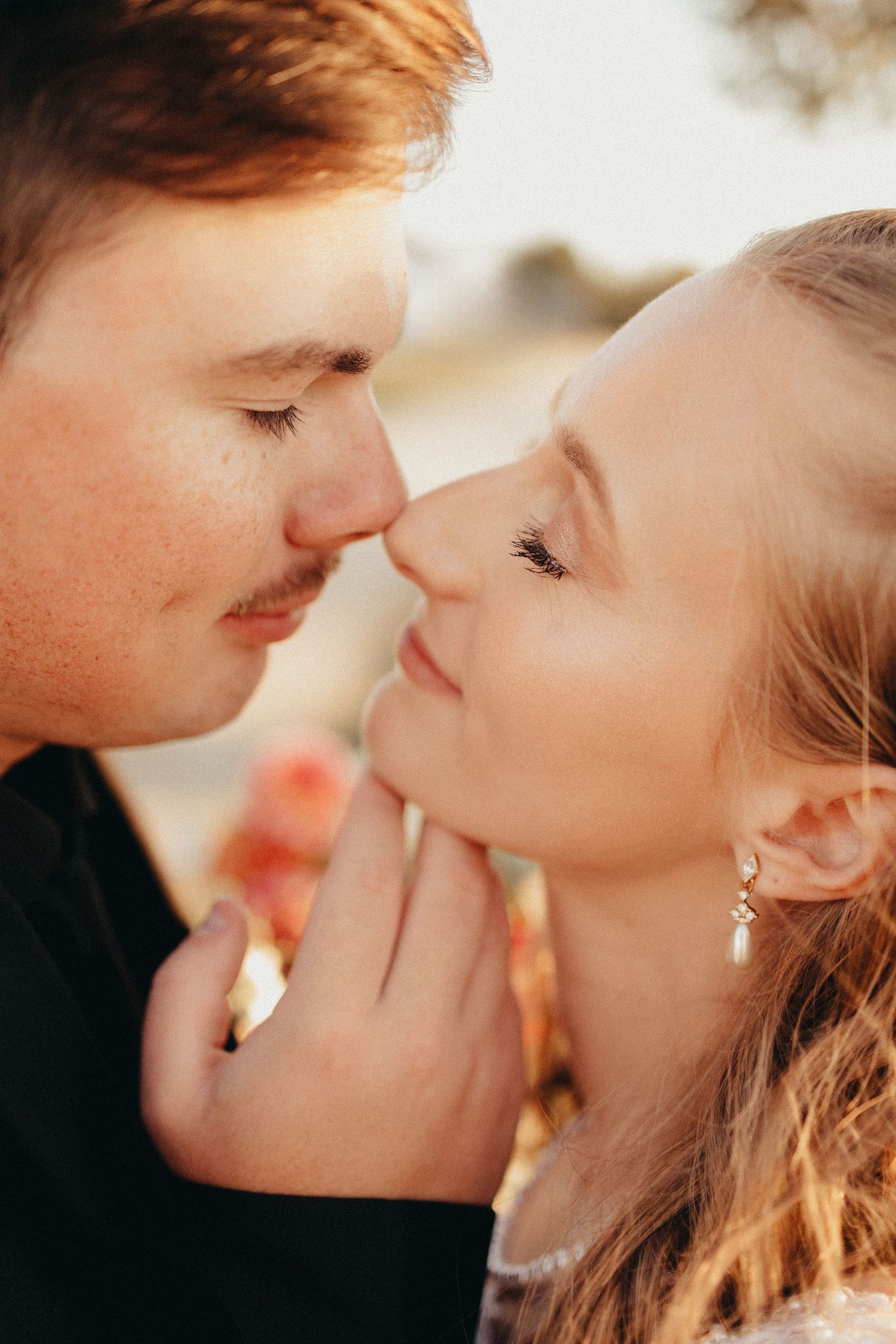 Close-up of groom gently kissing brides nose outdoors in warm golden light on their wedding day.