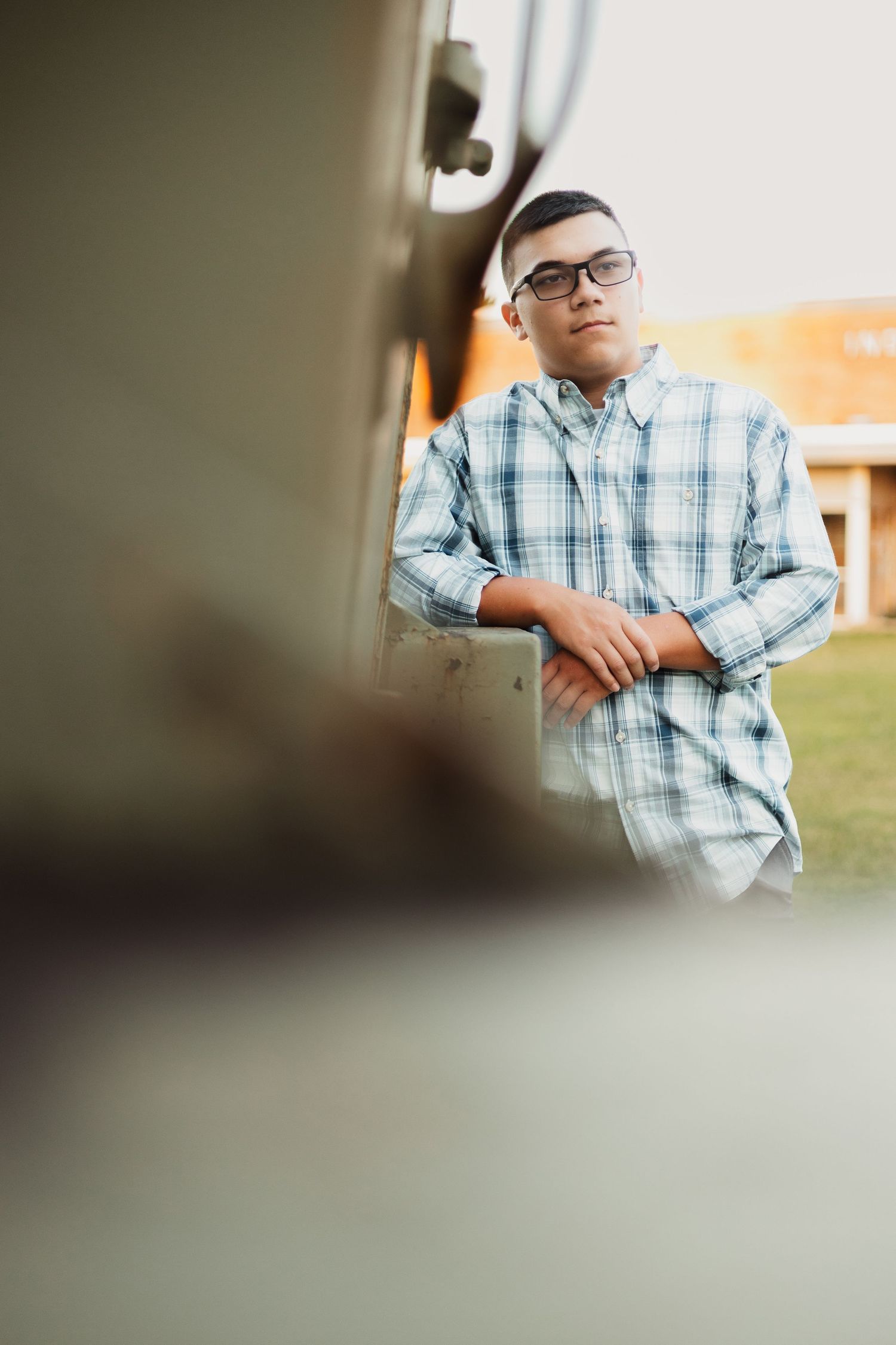 Teen boy in plaid shirt leaning against vintage vehicle for senior portrait.
