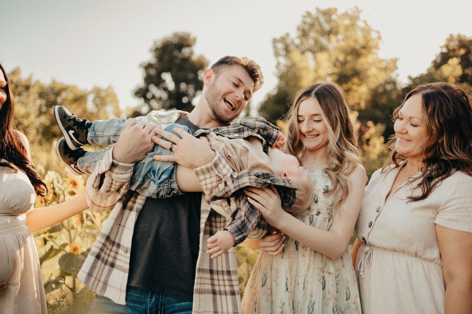 Joyful family group laughing together outdoors in a sunlit field with sunflowers.