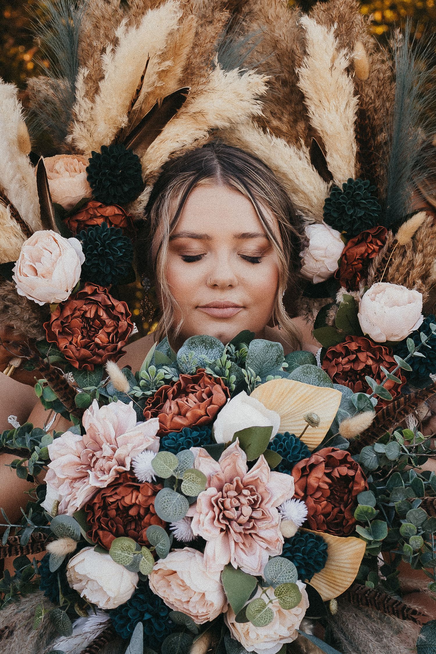 Bride surrounded by bohemian floral arrangement with pampas grass, peonies, and dahlias in earthy tones.