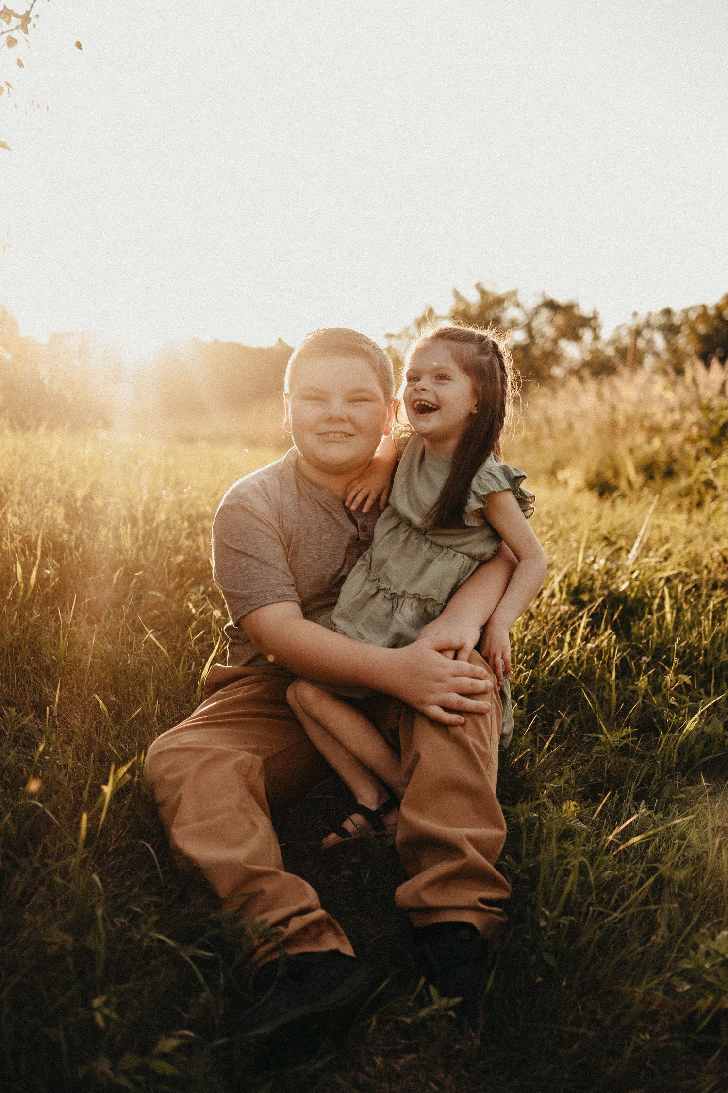 Smiling boy and girl siblings hugging in a golden sunlit grassy field.