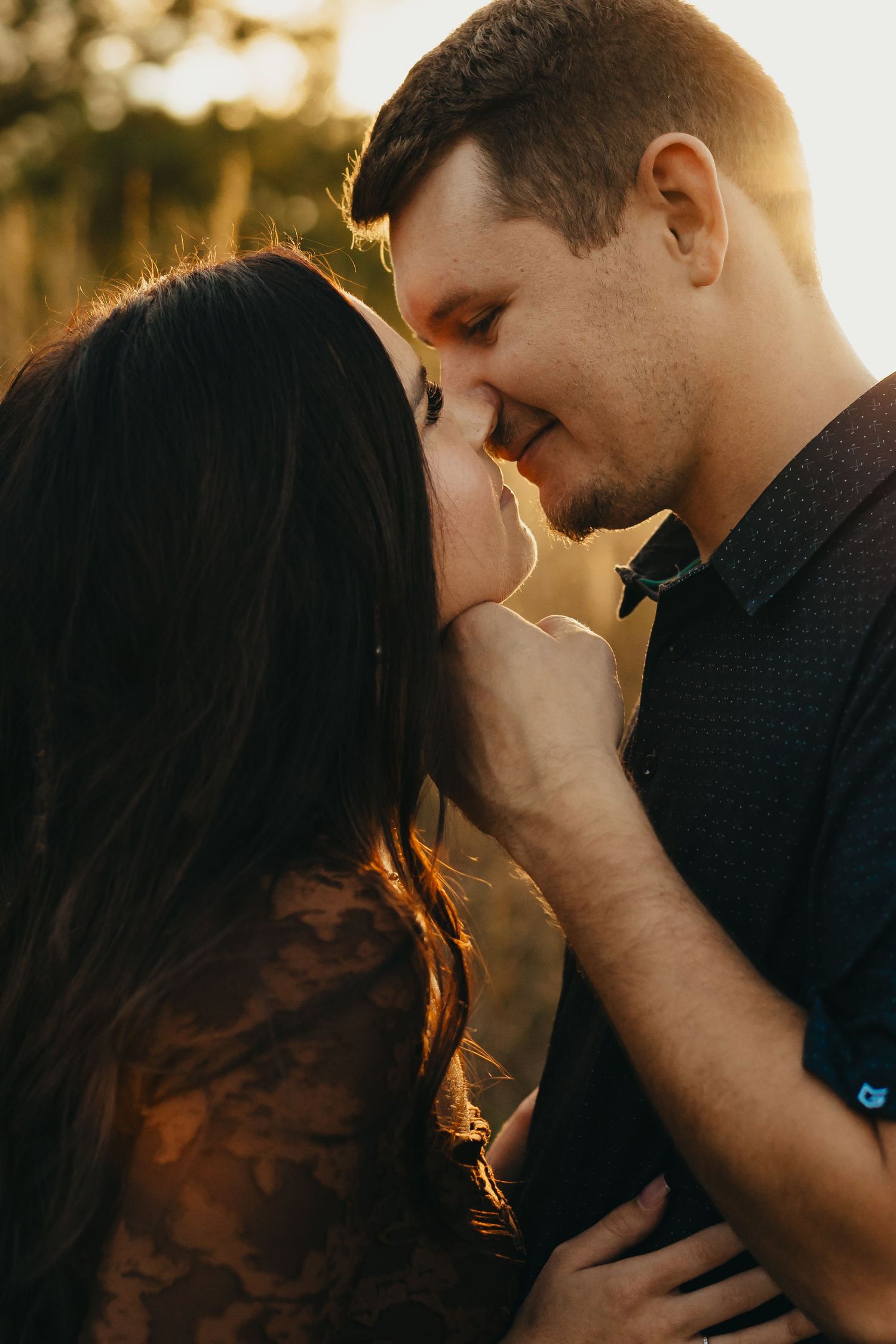 Romantic couple sharing an intimate moment at golden hour, a man gently holding a woman's chin as they nearly touch noses outdoors.
