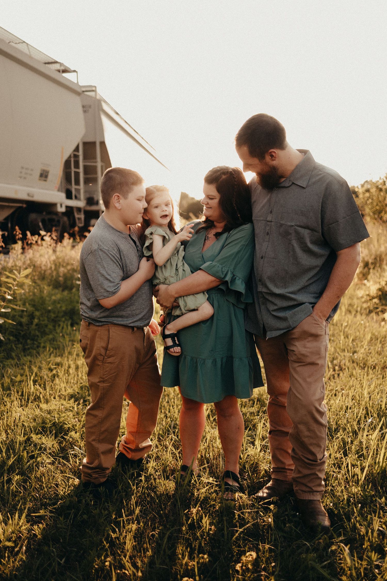 Happy family of four sharing a joyful moment in a golden sunlit field.