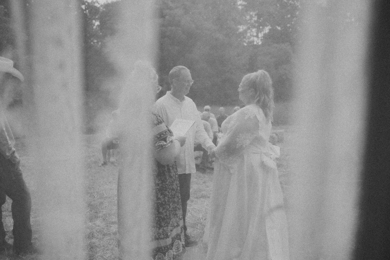 Black and white film photo of bride and groom exchanging vows at outdoor wedding ceremony.