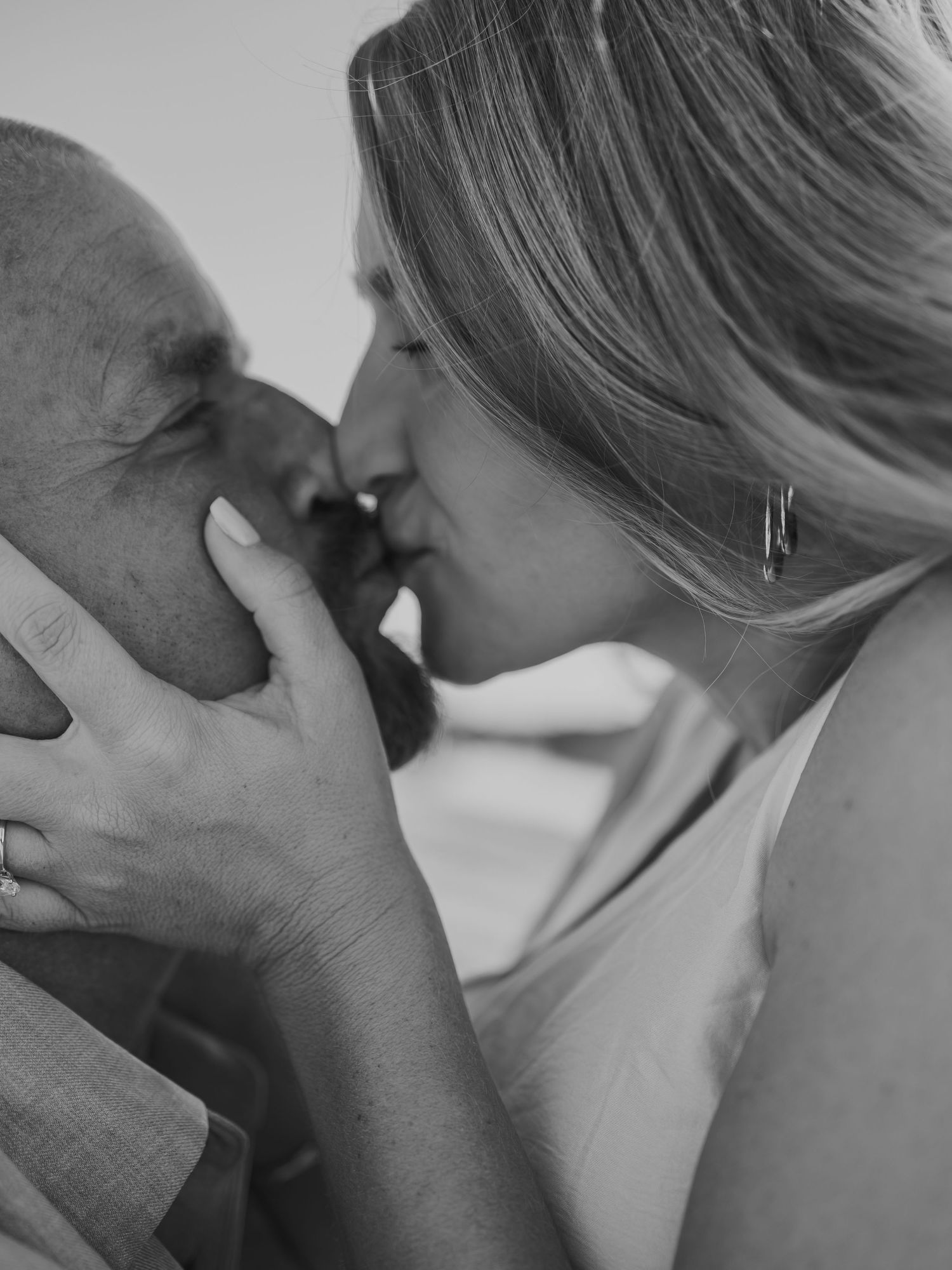 Black and white photo of a couple sharing a tender kiss, woman with blonde hair wearing a ring and earring.