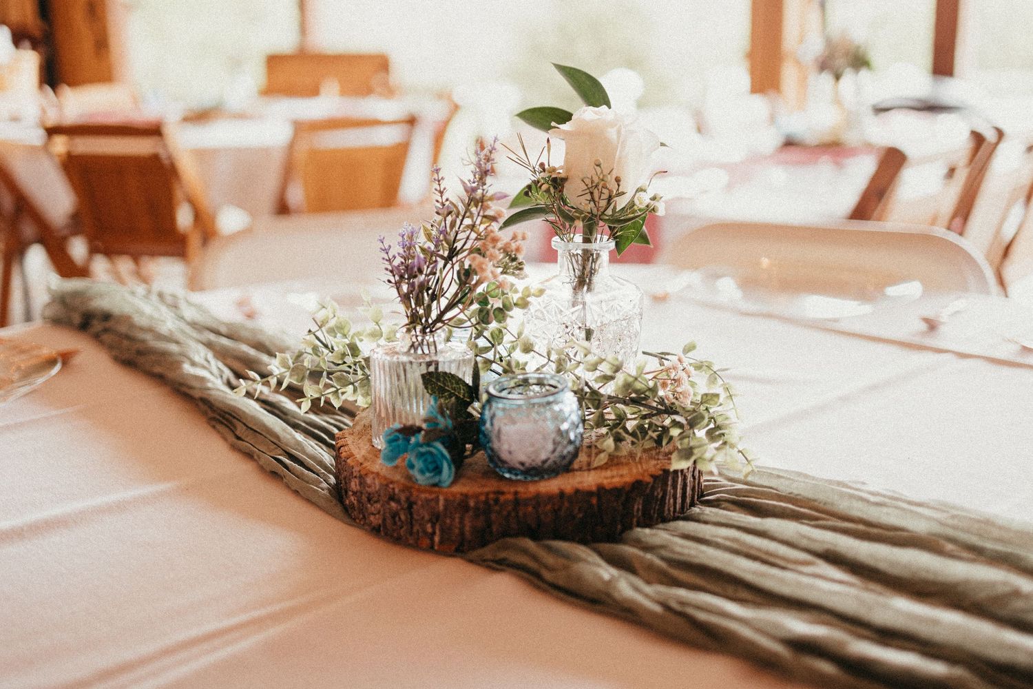 Rustic wedding reception table centerpiece with wildflowers and candles on wood slice runner.