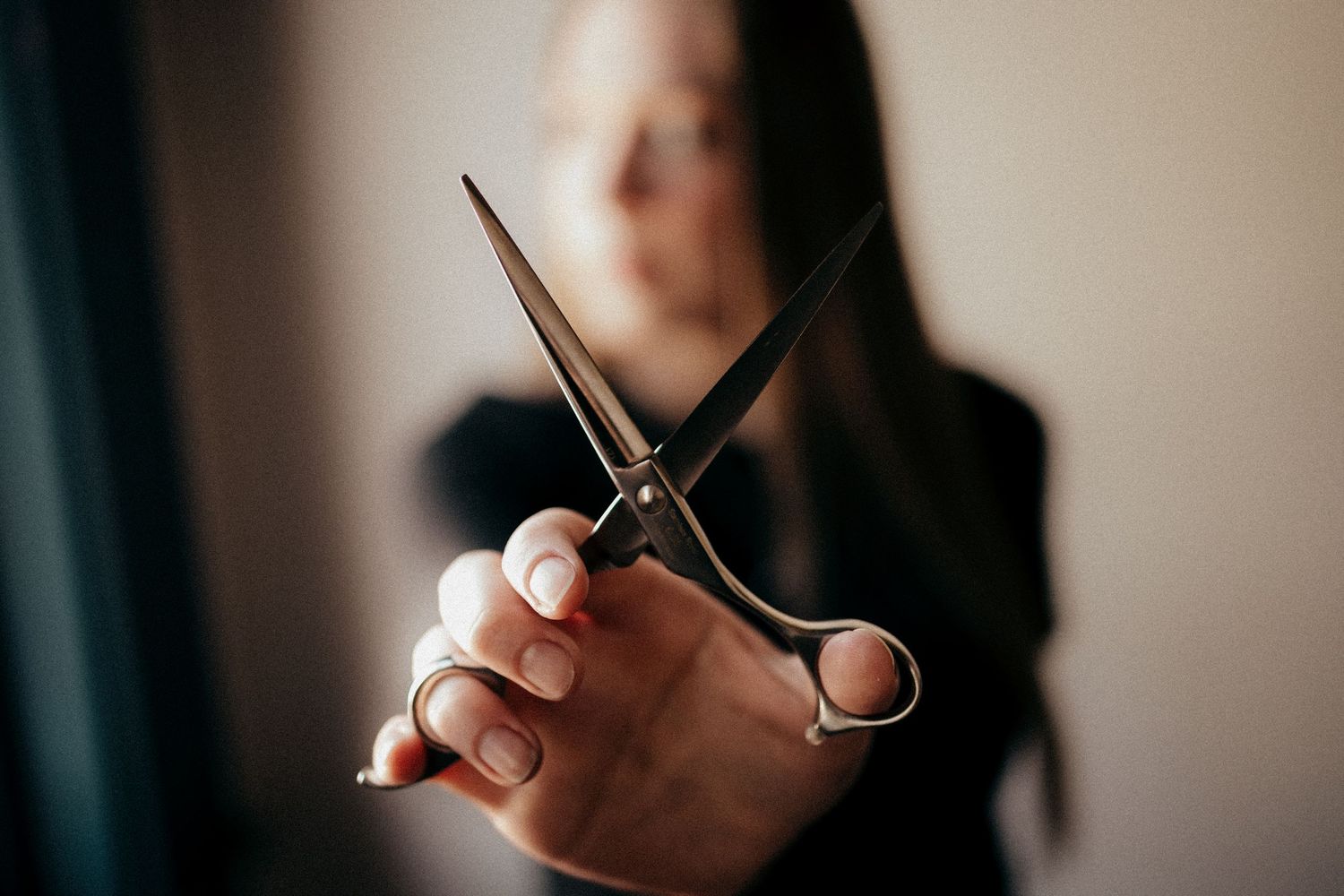 Woman holding professional hair scissors toward camera in a blurred background.