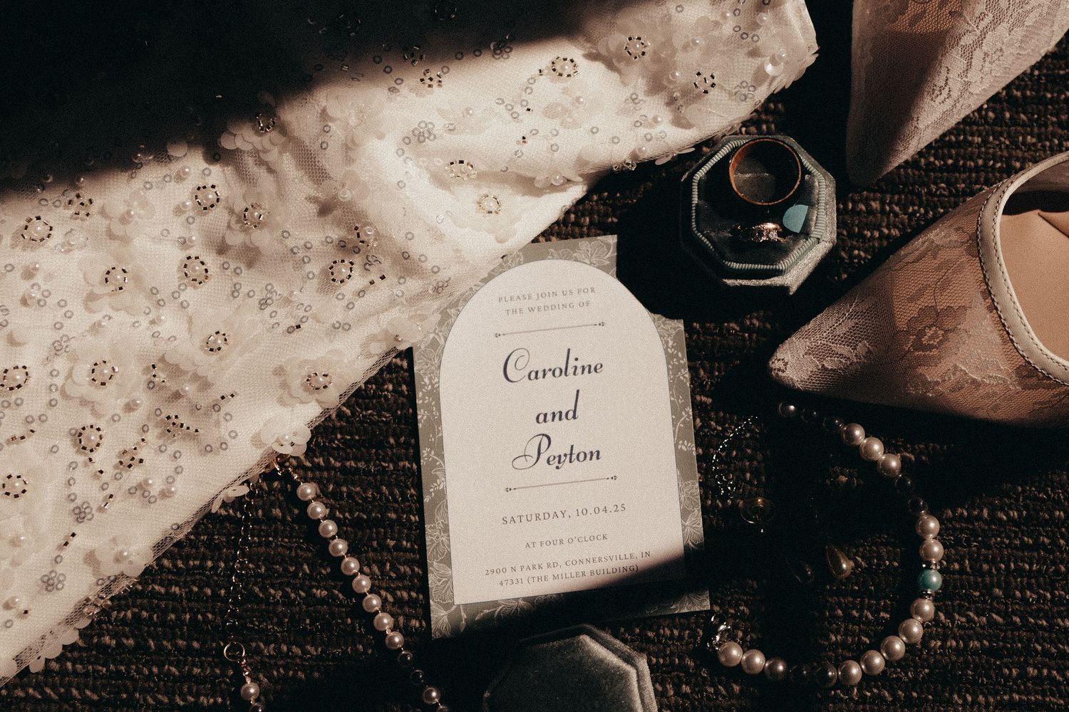 Flat lay of wedding invitation for Caroline and Peyton surrounded by rings, pearls, and bridal accessories.