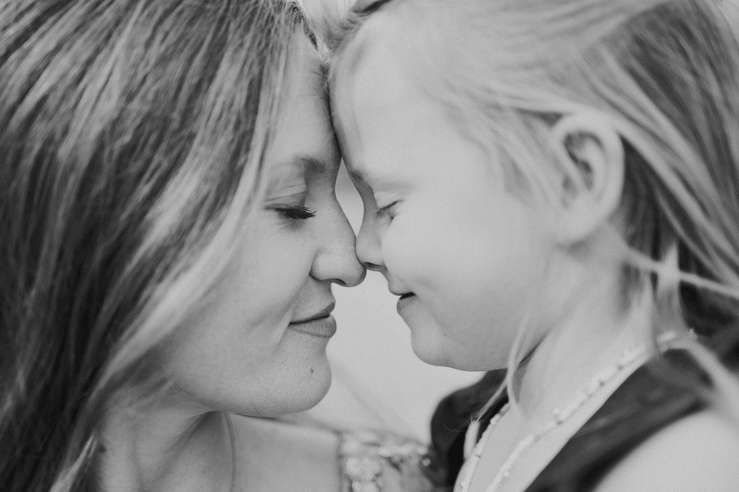 Black and white close-up of a mother and daughter touching foreheads and smiling together.