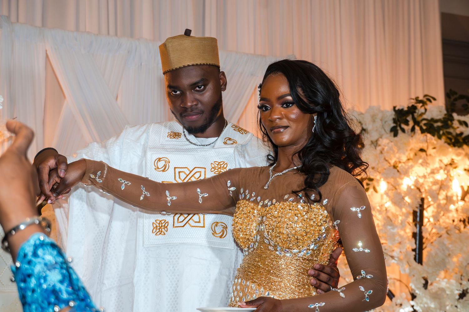 Bride and groom in traditional wedding attire celebrating at their reception with a floral backdrop