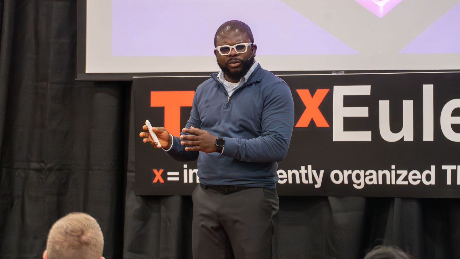 Man speaking on stage at a TEDx event, gesturing while presenting