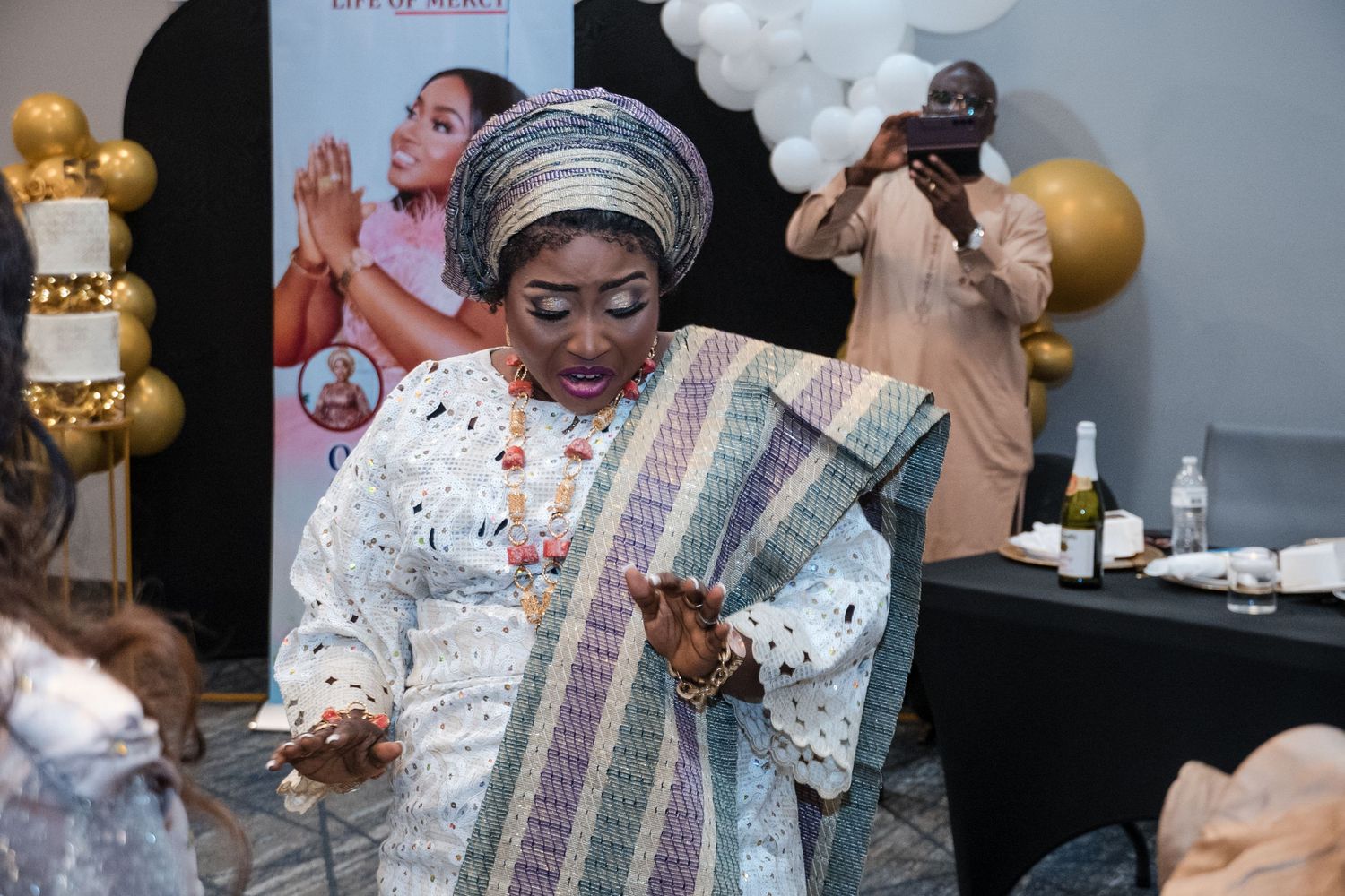 Woman in traditional attire and headwrap dancing at a celebration with balloon decor