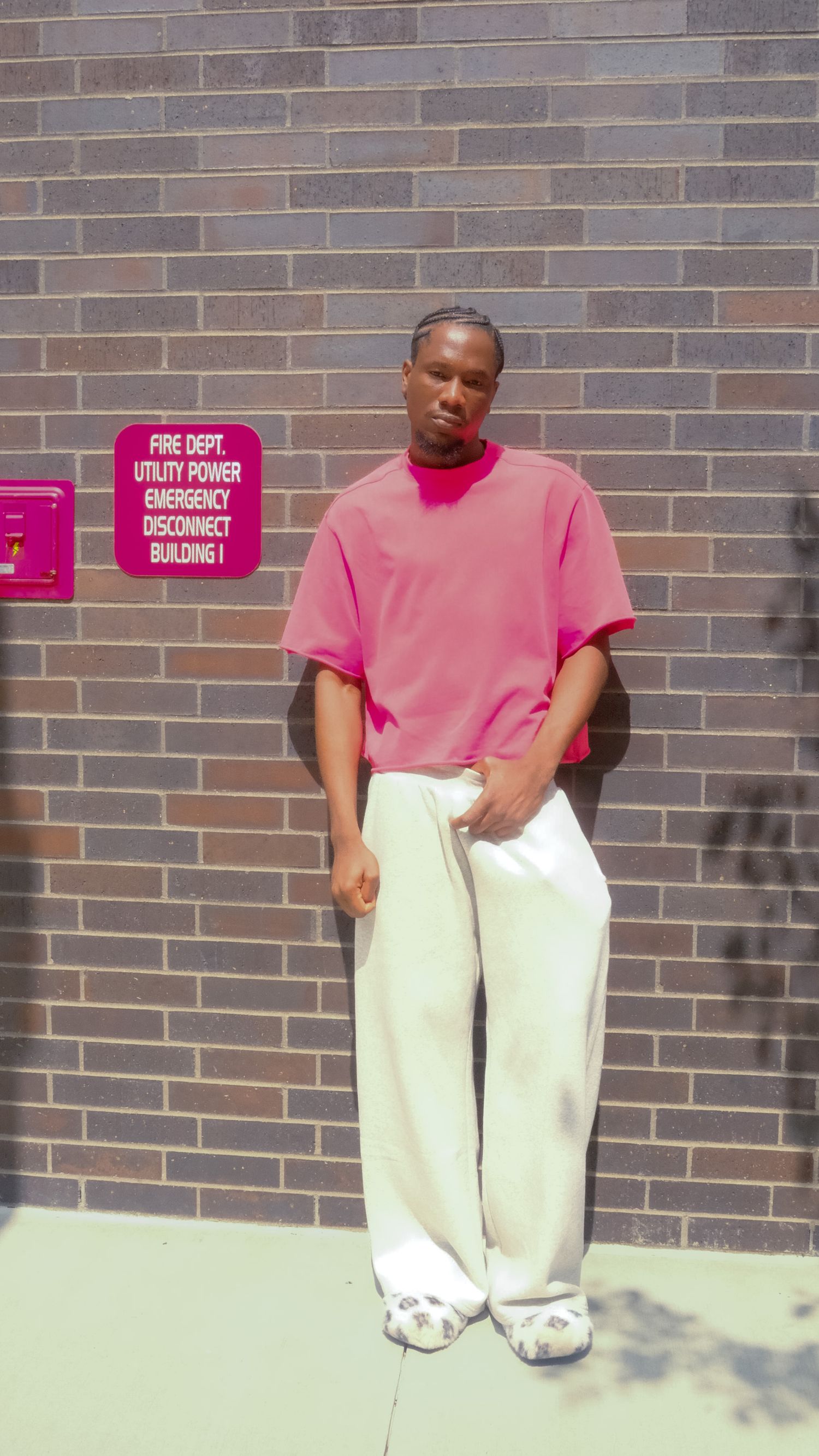 Man in a pink polo shirt and white pants standing against a brick wall