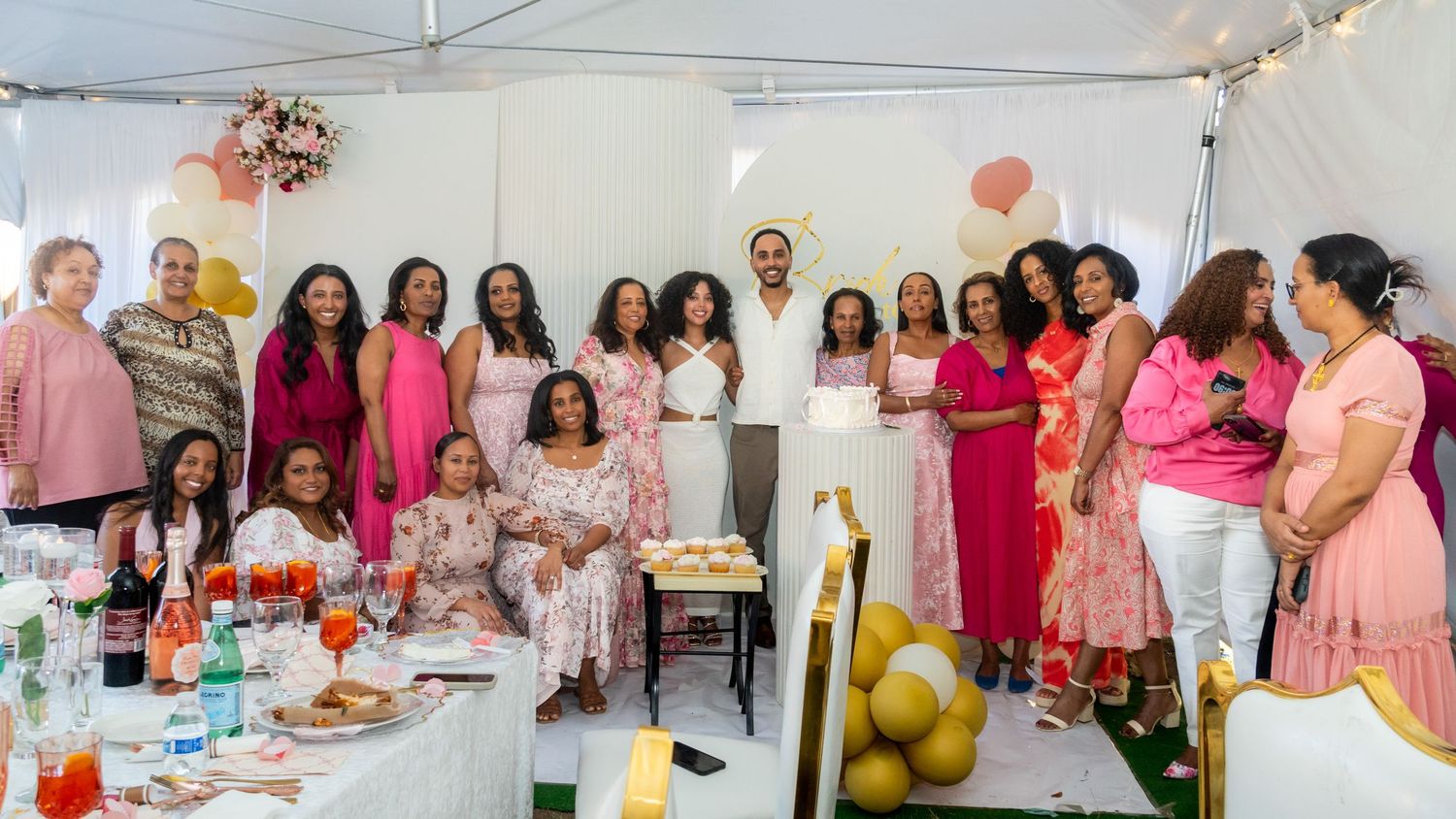 Large group posing together at a bridal shower celebration with pink decor and balloons