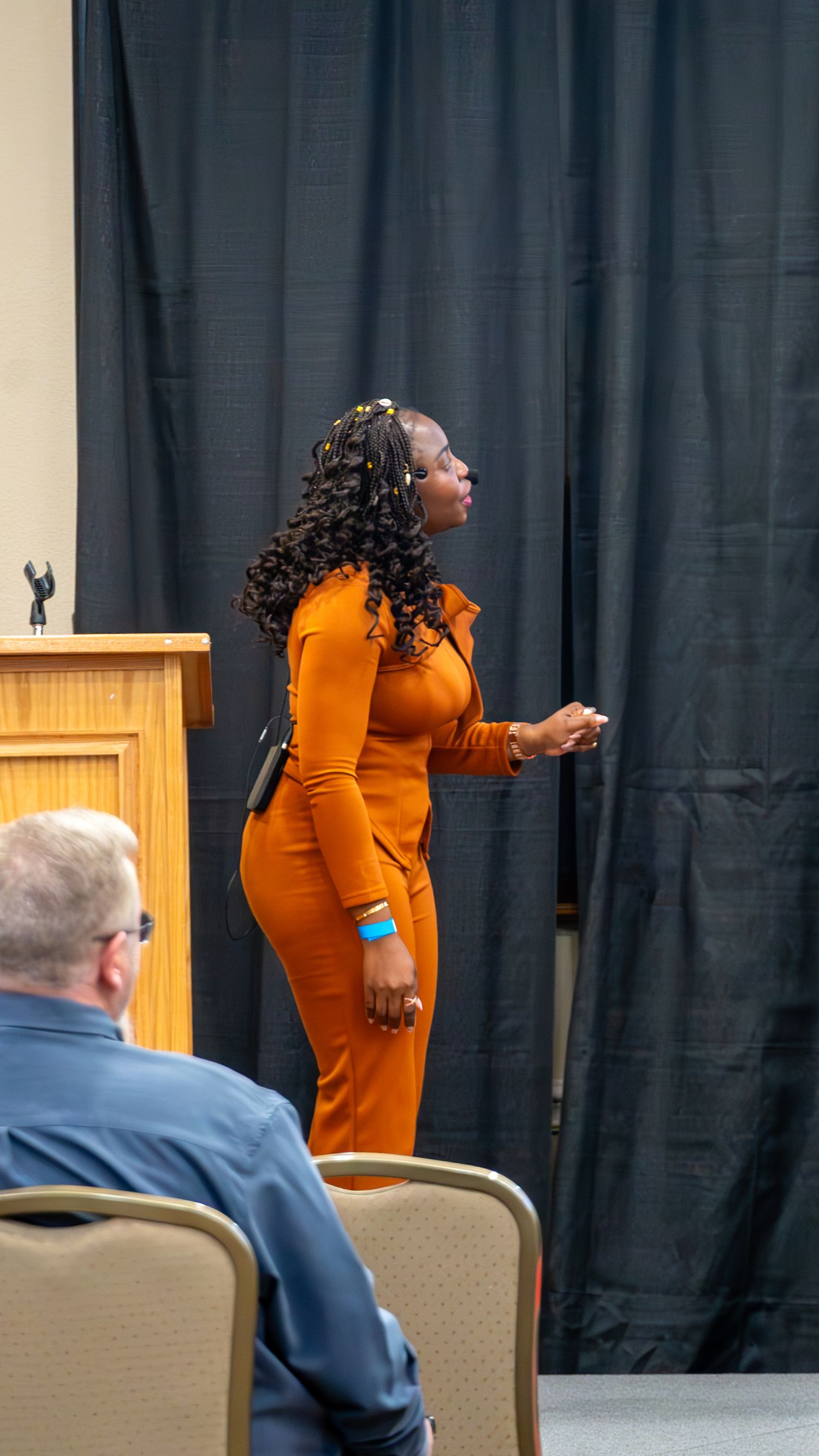 Woman in an orange outfit speaking on stage at a TEDx event