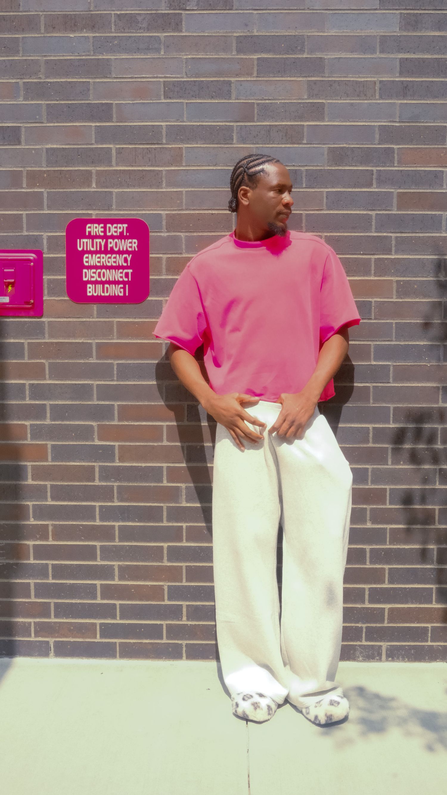 Man in a pink polo shirt and white pants posing against a brick wall