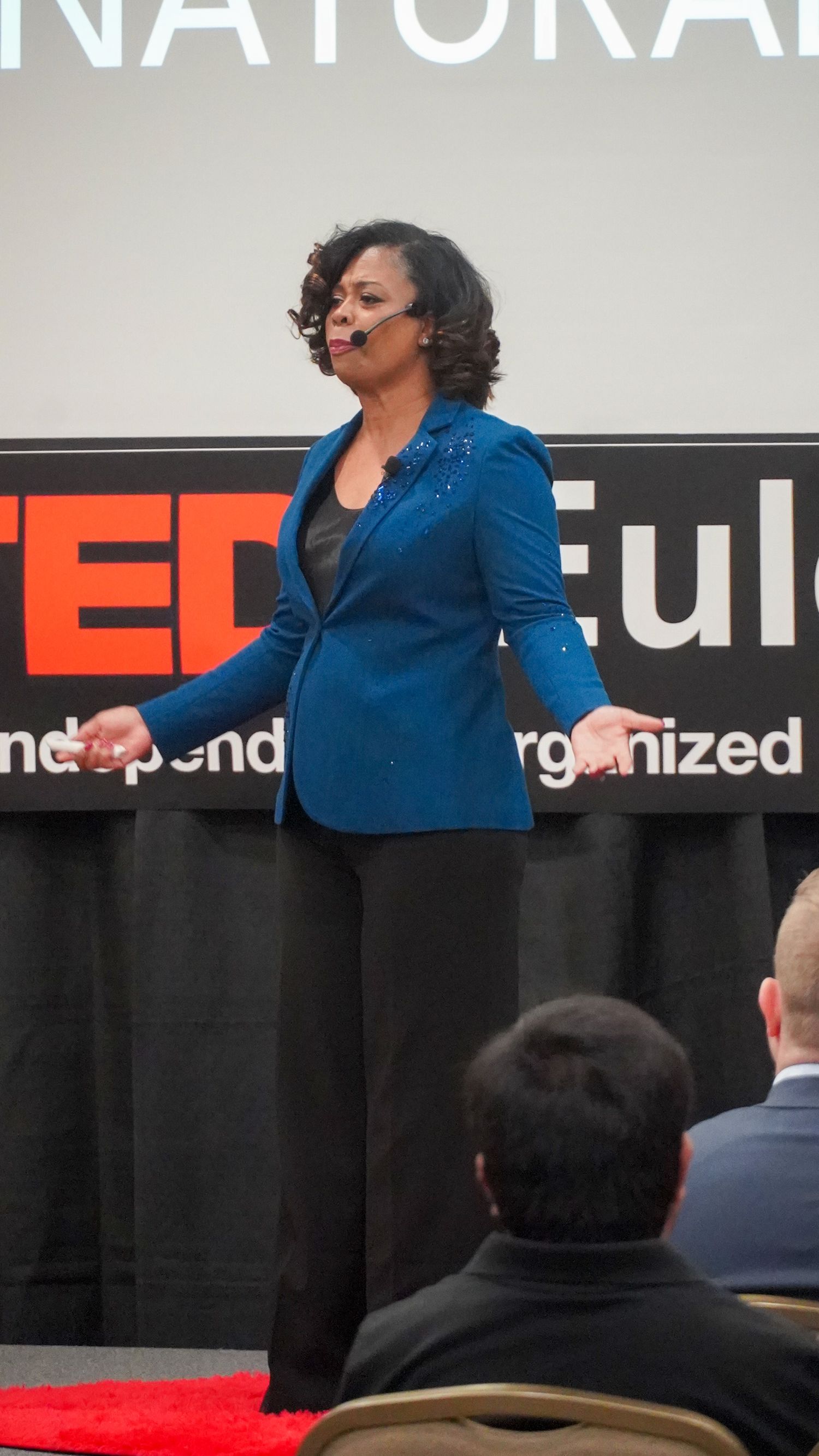 Woman in a blue blazer speaking on stage at a TEDx event
