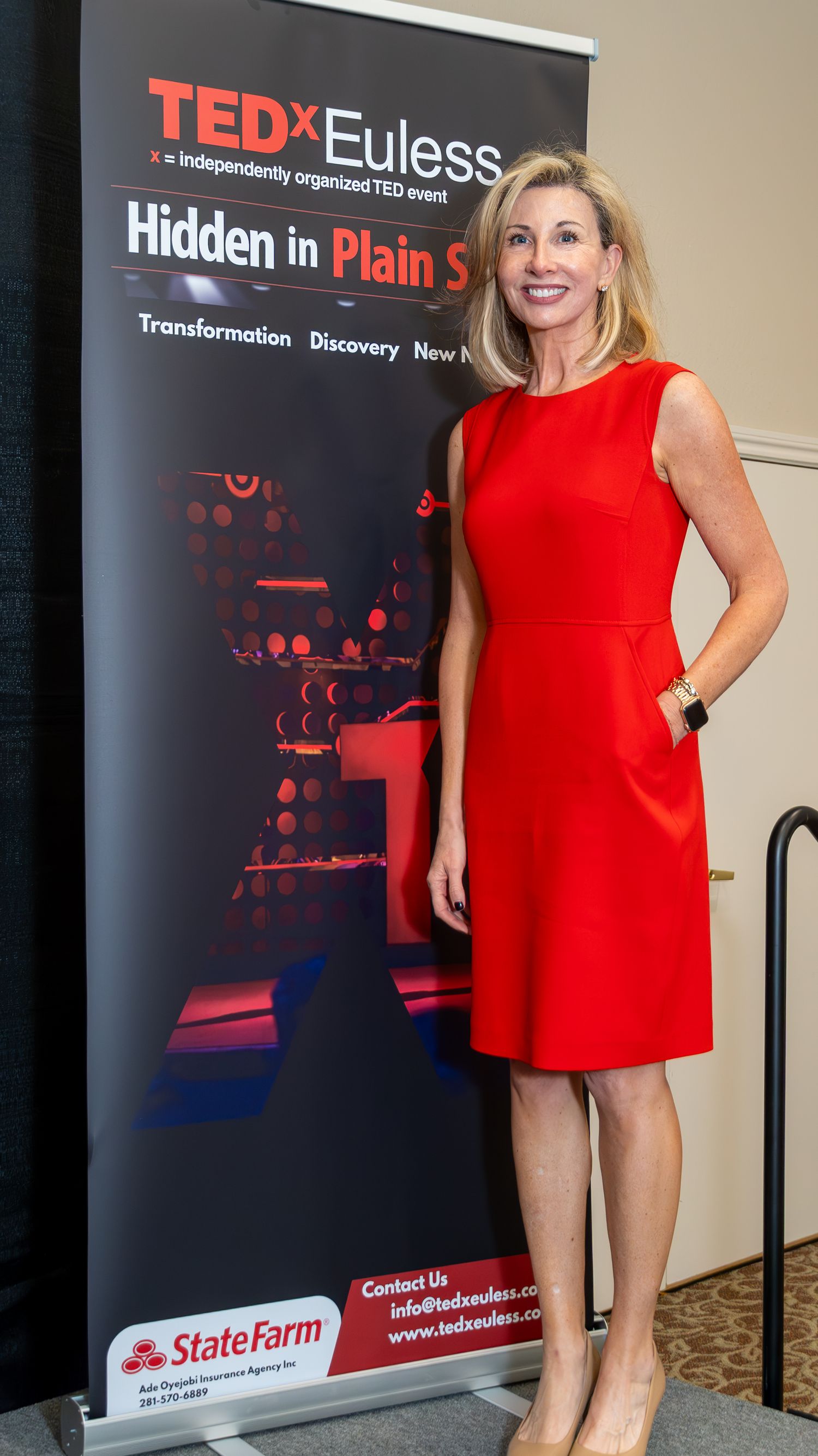 Woman in a red dress posing beside a TEDx event banner